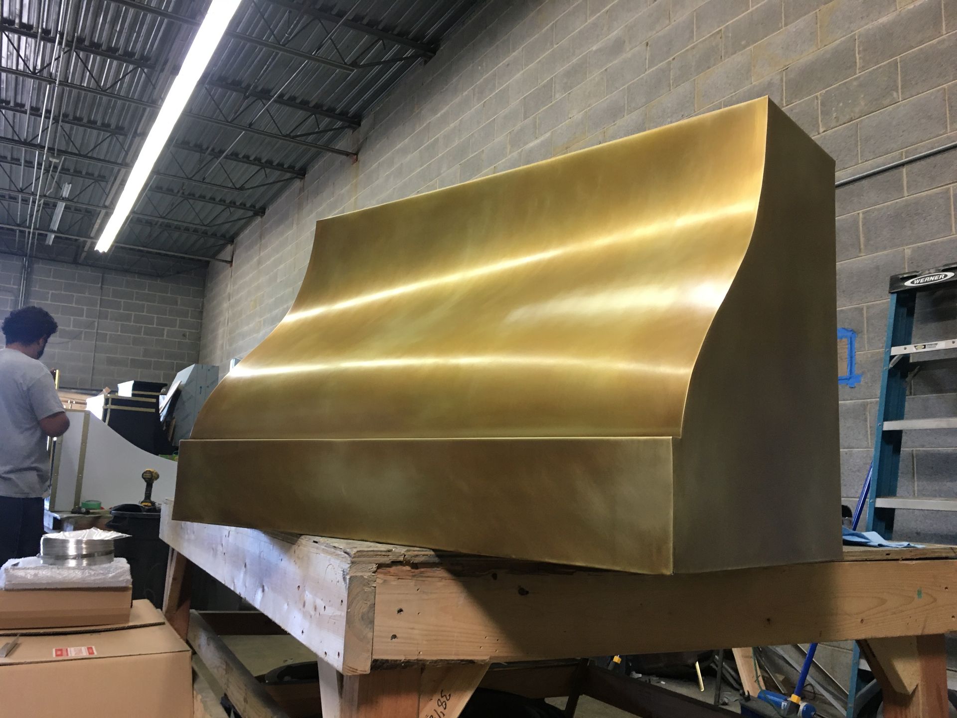 A brass hood is sitting on a wooden table in a warehouse.