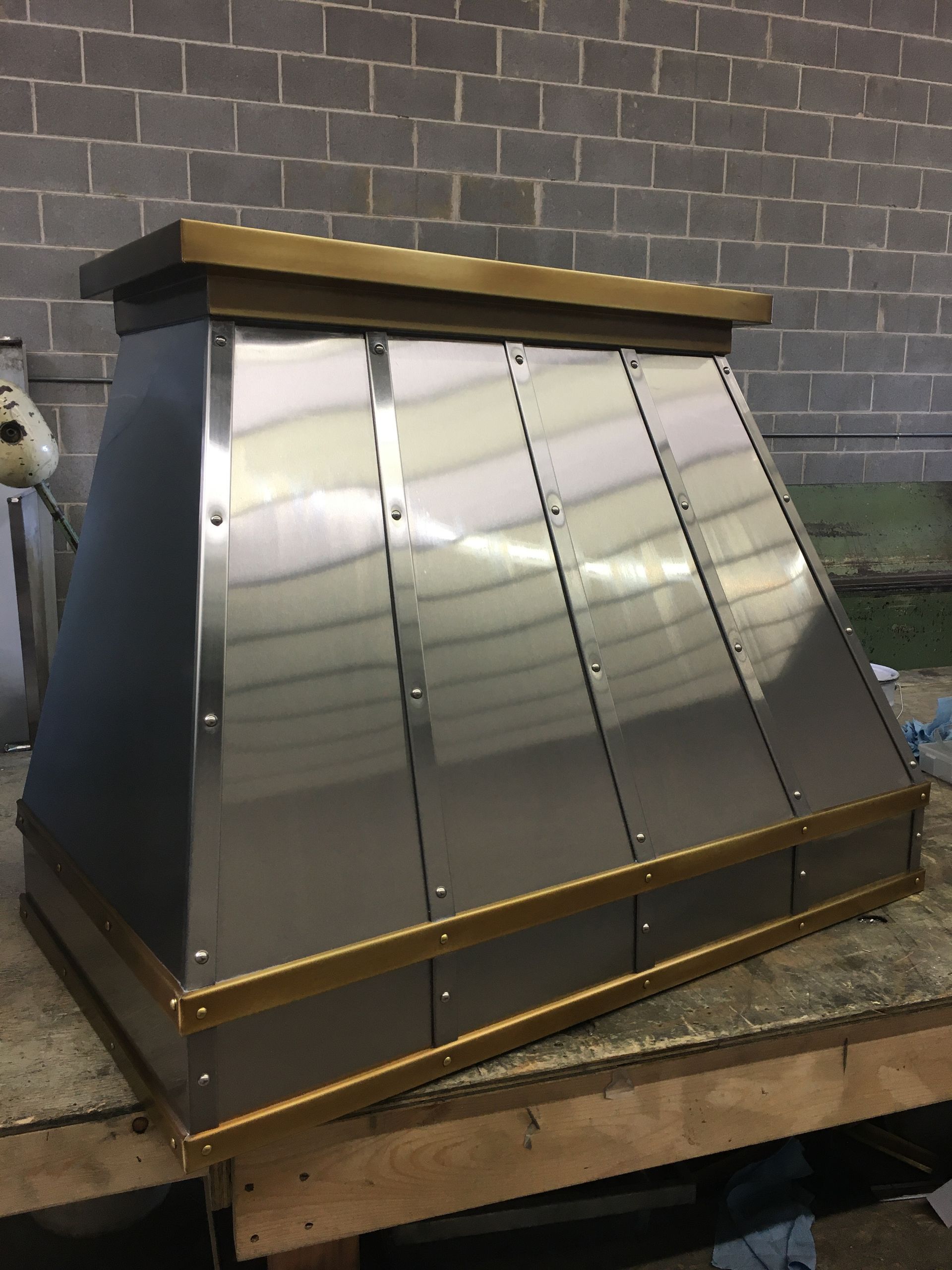 A stainless steel hood is sitting on a wooden table in front of a brick wall.