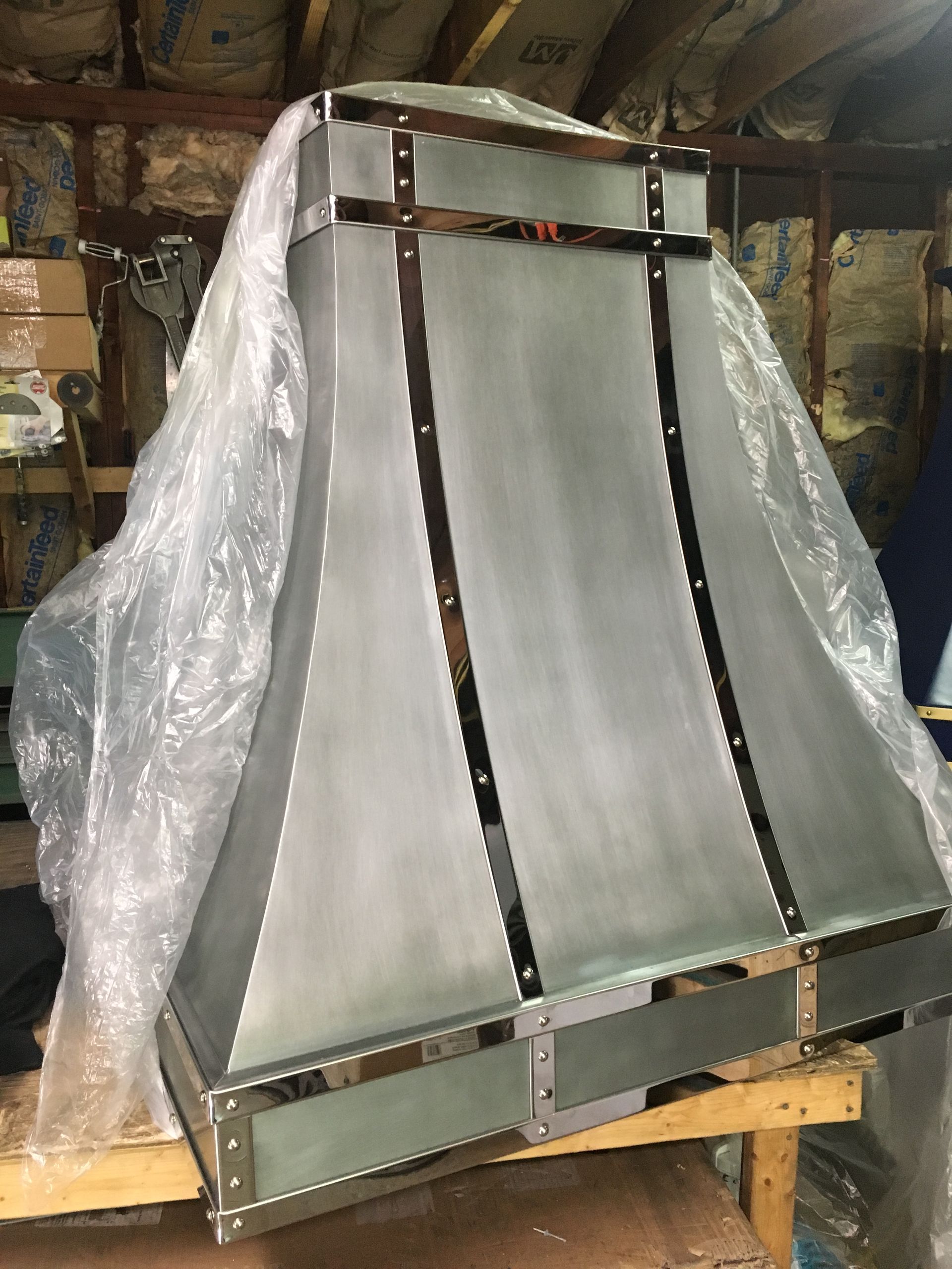 A stainless steel hood is wrapped in plastic and sitting on a wooden table.