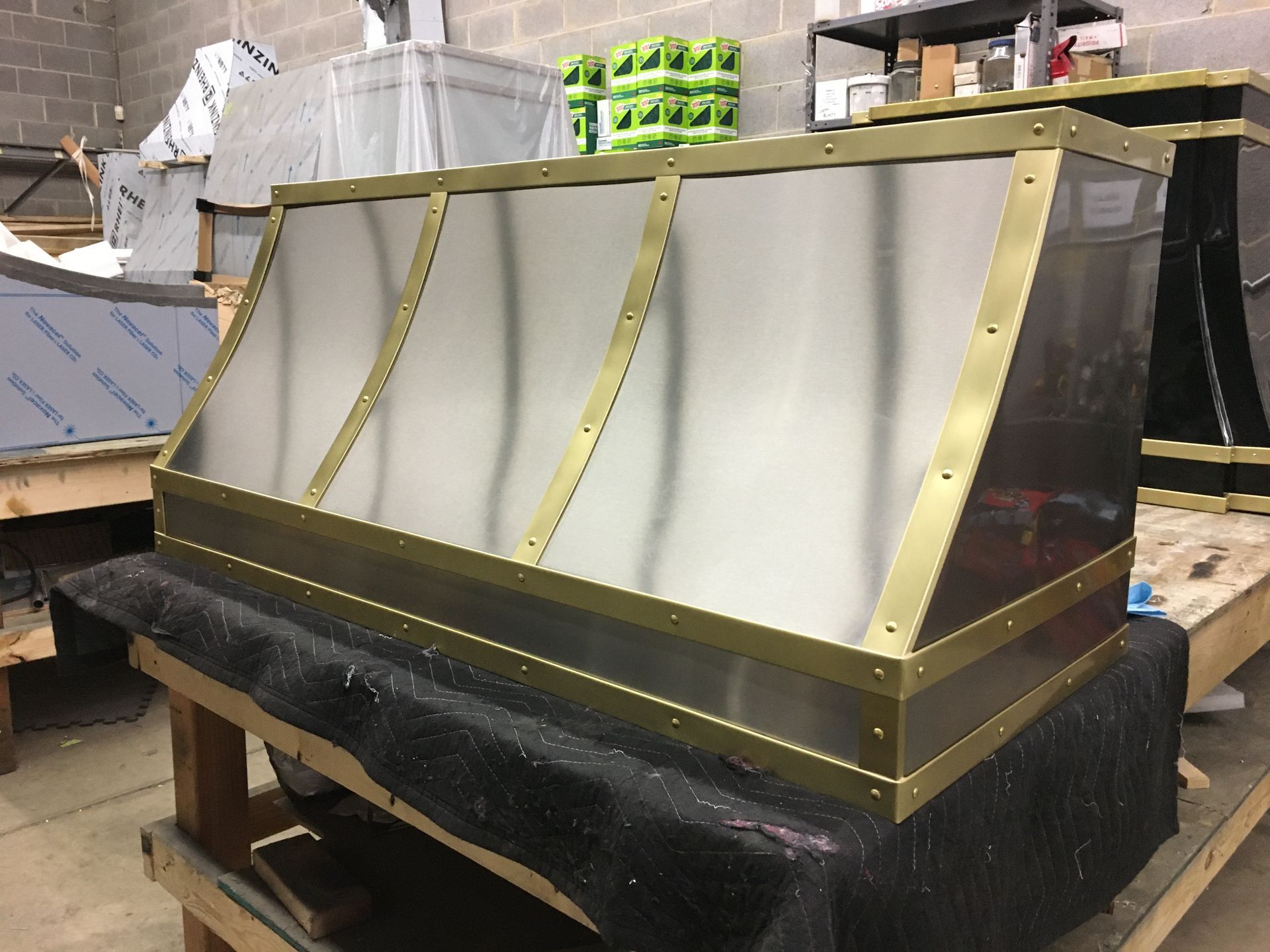 A stainless steel hood with brass trim is sitting on a wooden table.