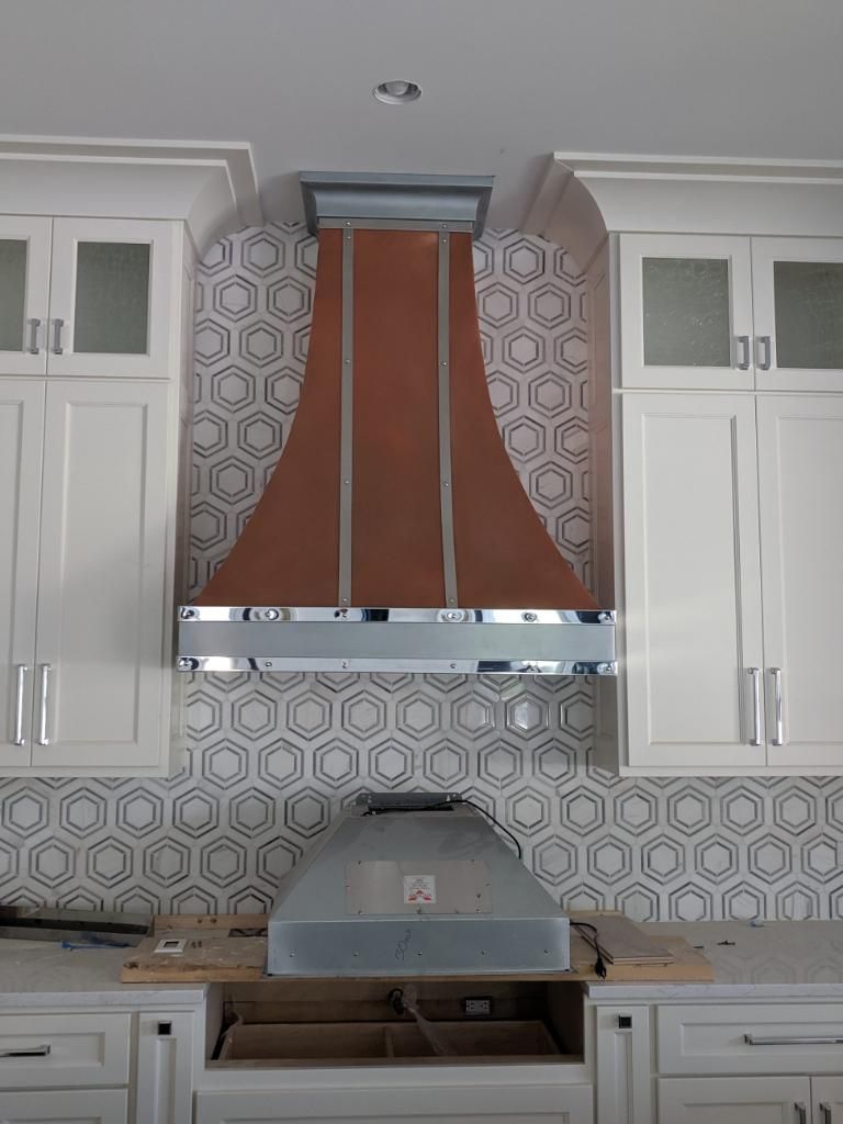 A kitchen with white cabinets and a copper hood hanging from the ceiling.