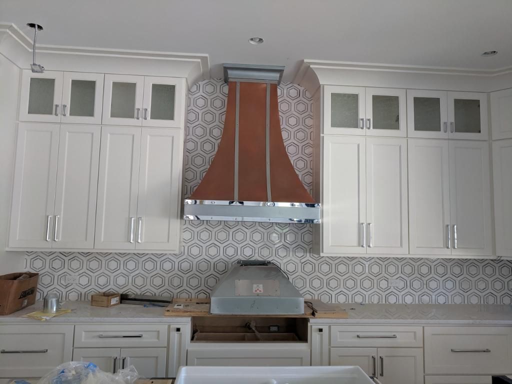 A kitchen with white cabinets and a copper hood