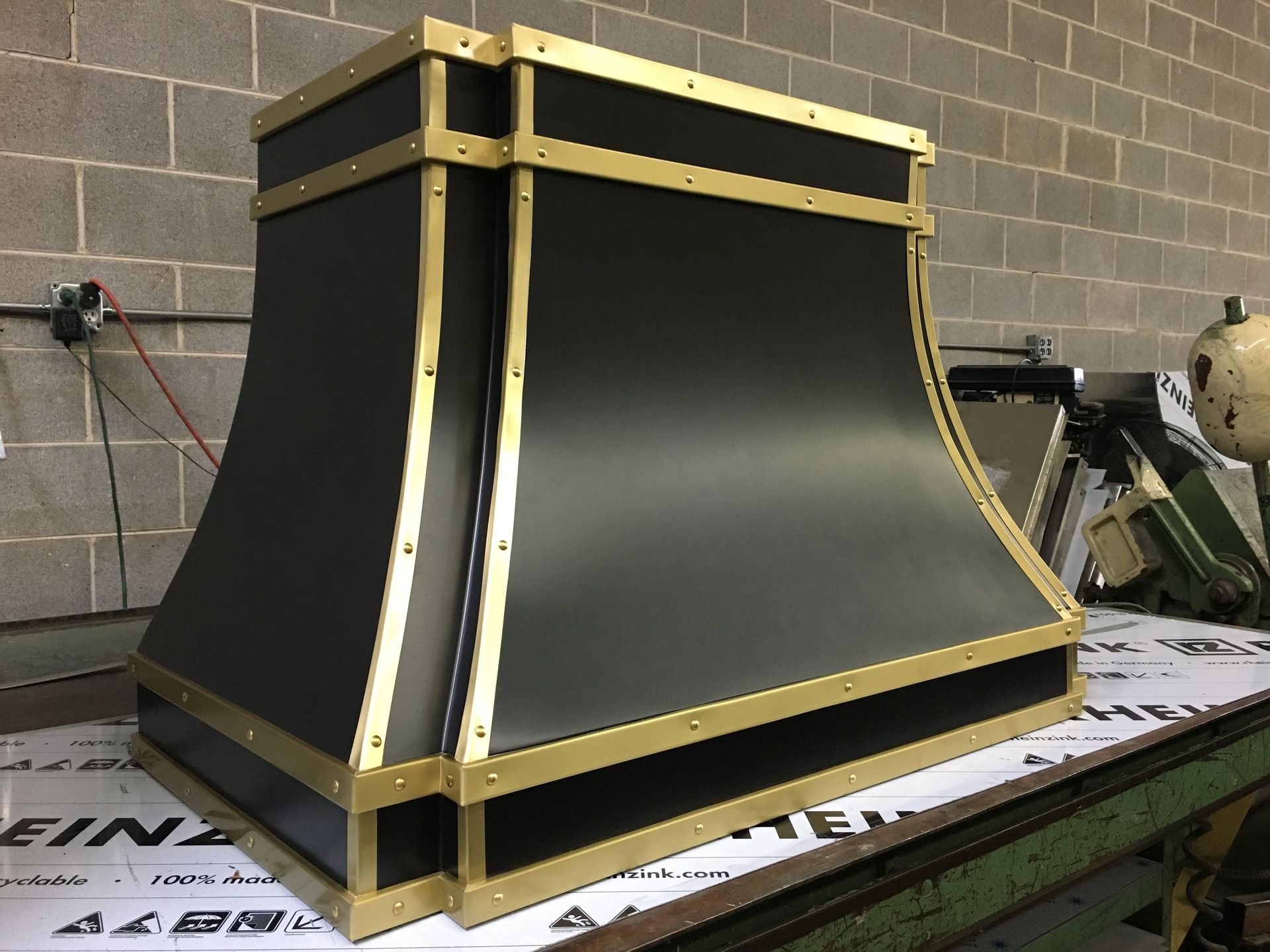 A black and gold hood is sitting on a table in front of a brick wall.