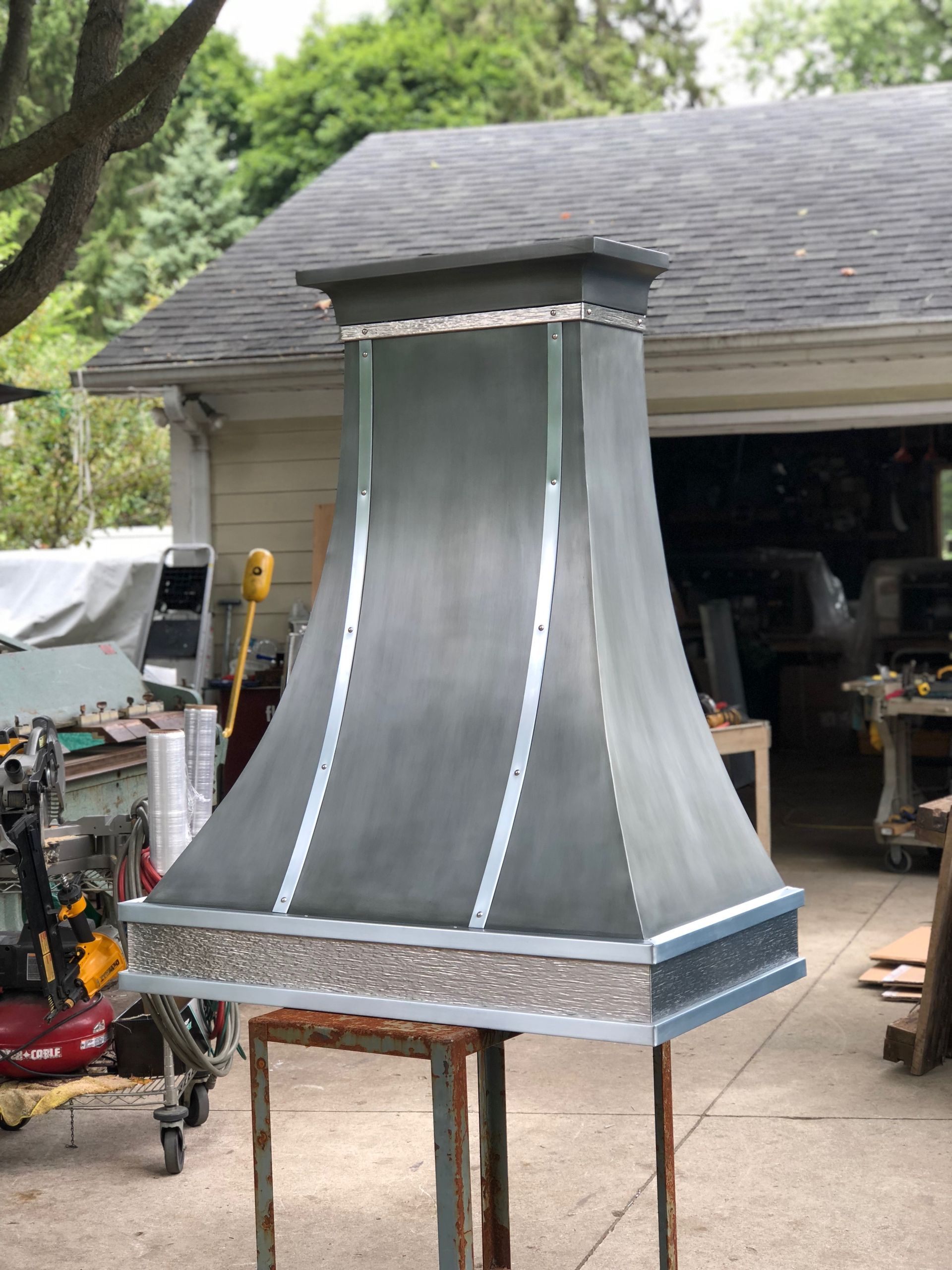 A metal hood is sitting on a wooden table in front of a garage.