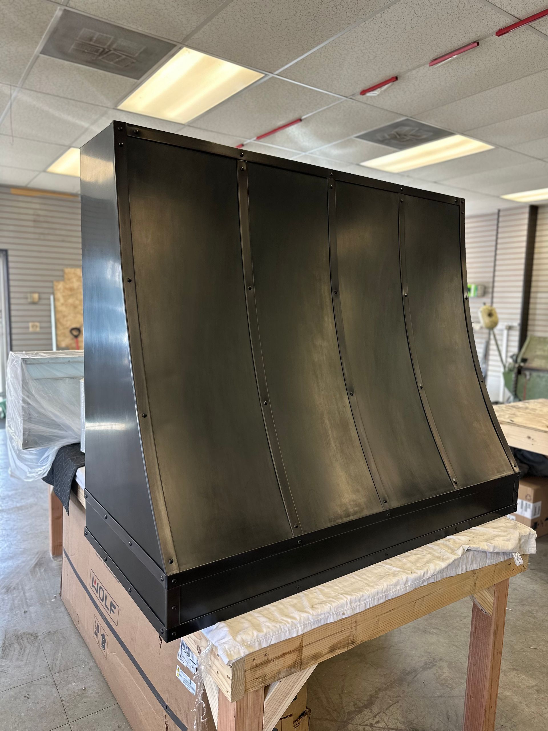 A black stainless steel hood is sitting on top of a wooden table in a room.
