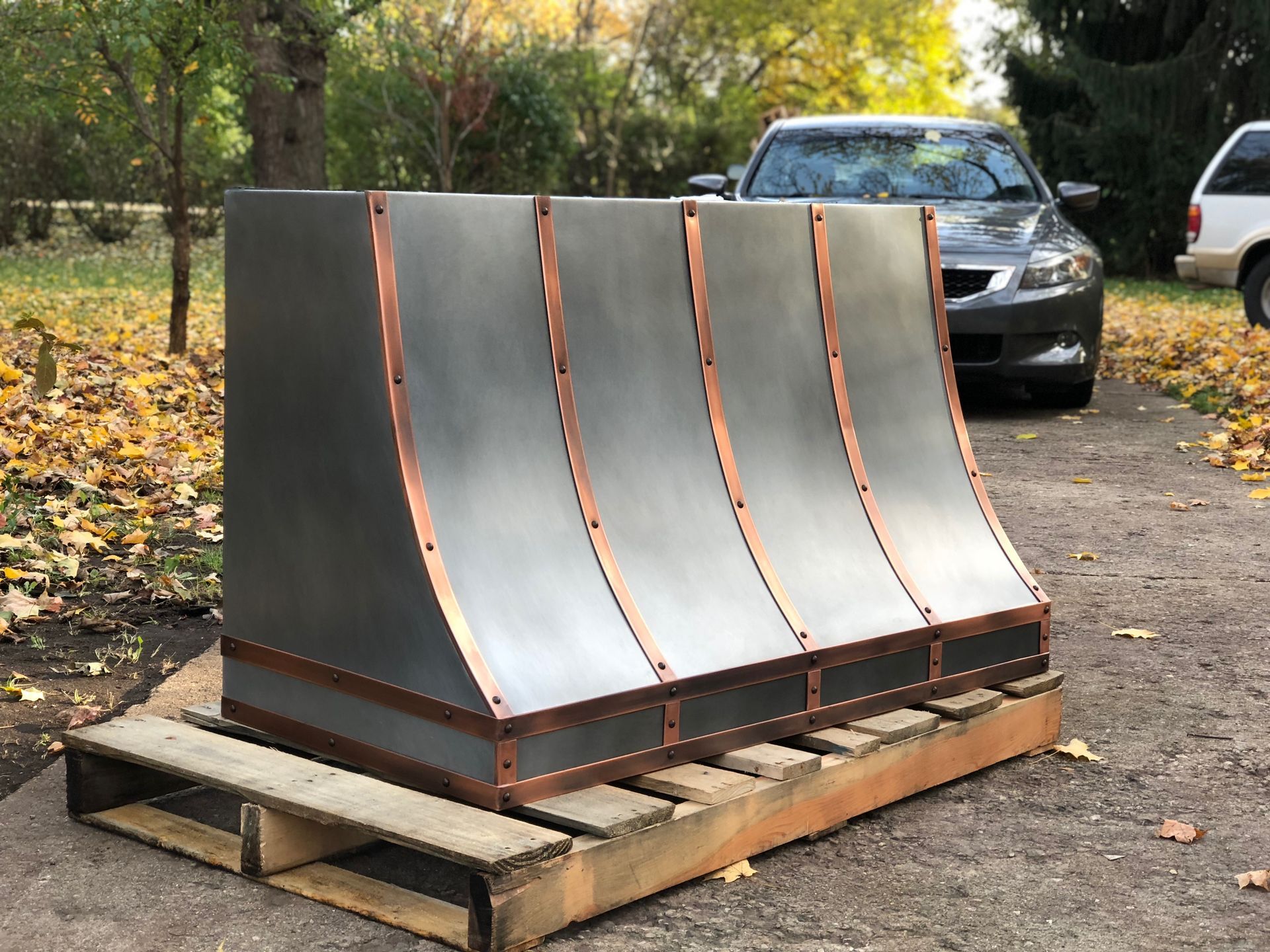 A car is parked in front of a large metal object on a wooden pallet.