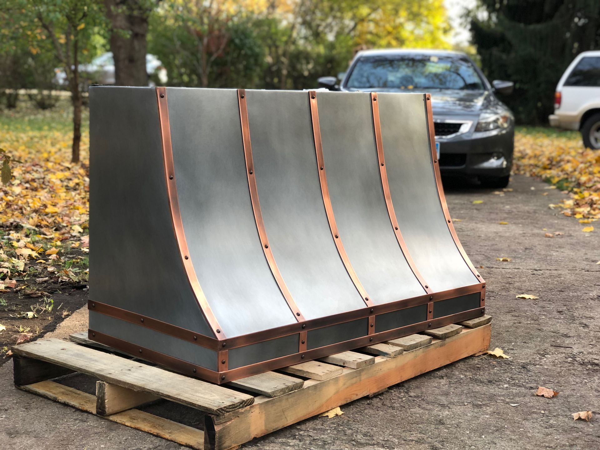 A metal and copper hood is sitting on a wooden pallet.