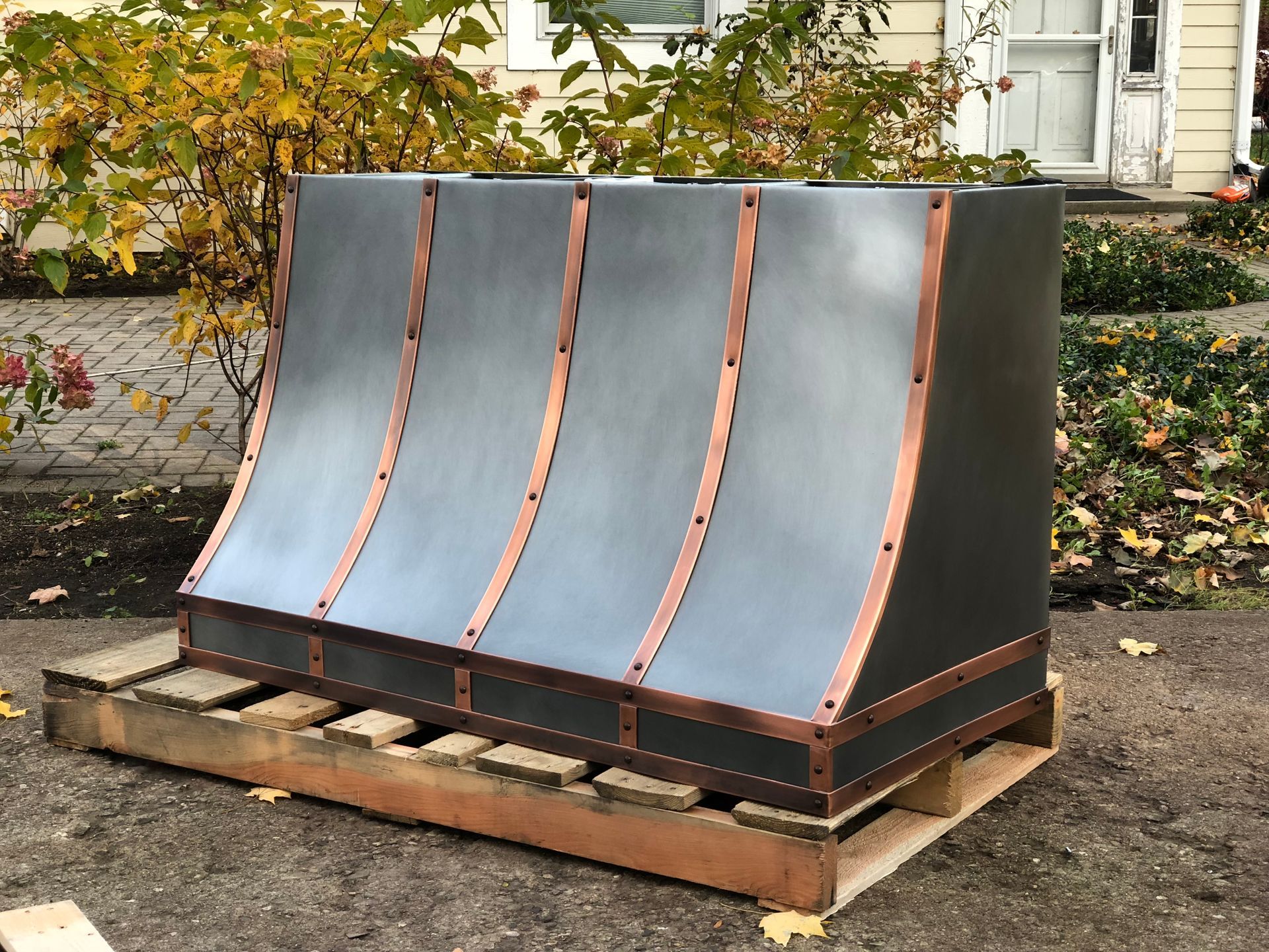 A black and copper hood is sitting on a wooden pallet in front of a house.