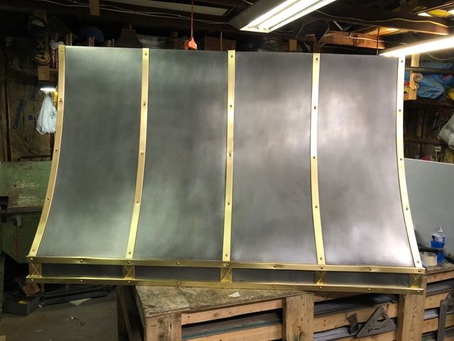 A stainless steel hood with brass trim is sitting on top of a wooden table.