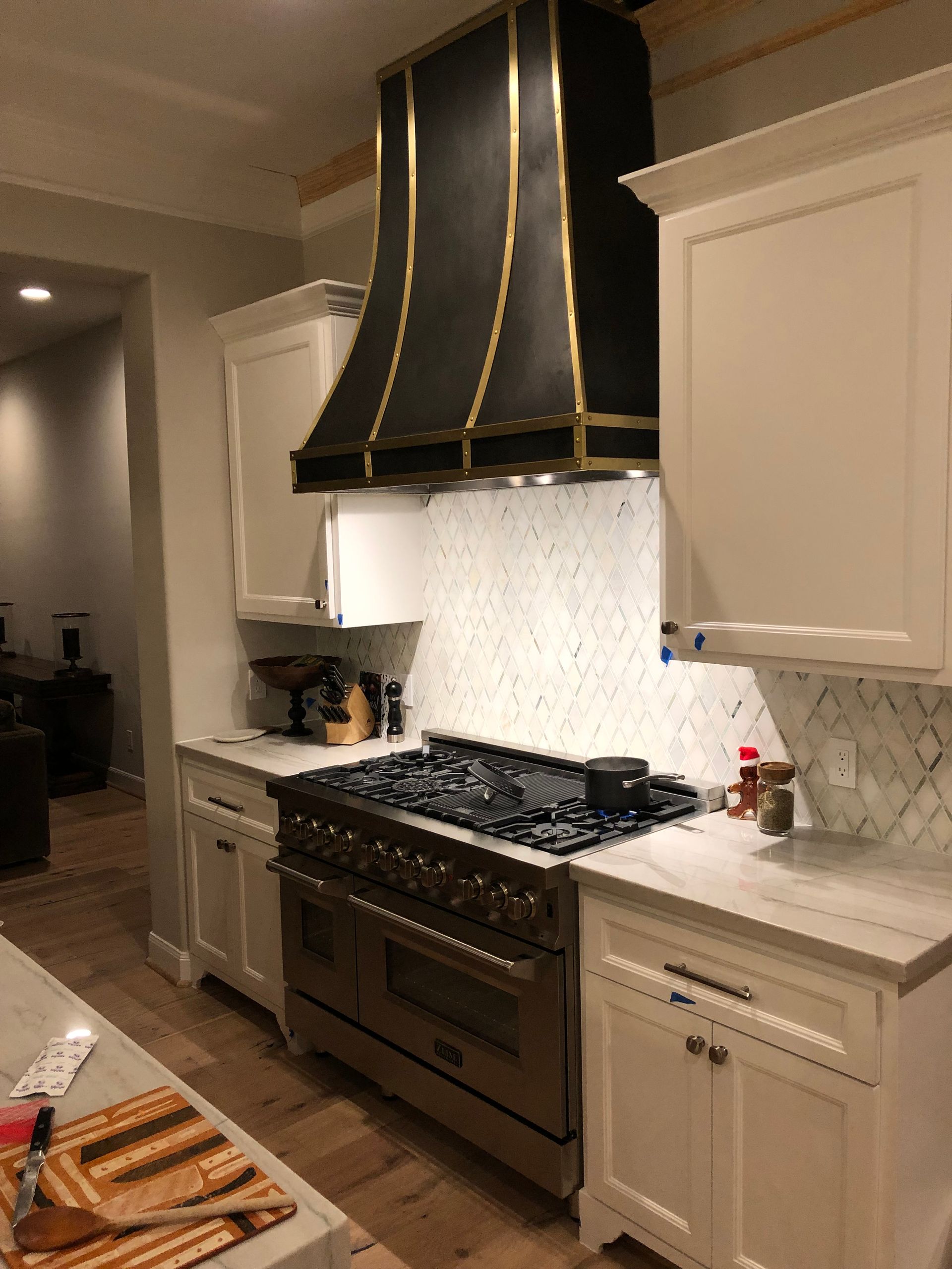 A kitchen with white cabinets , a stove top oven , and a black hood.