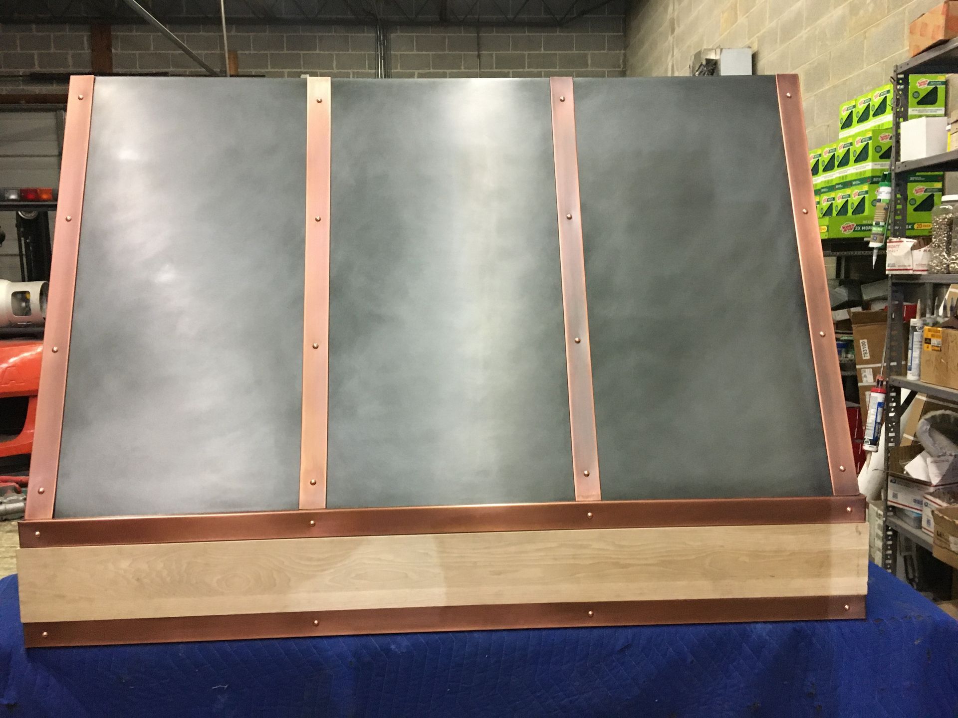 A copper hood with a wooden frame is sitting on a blue table.