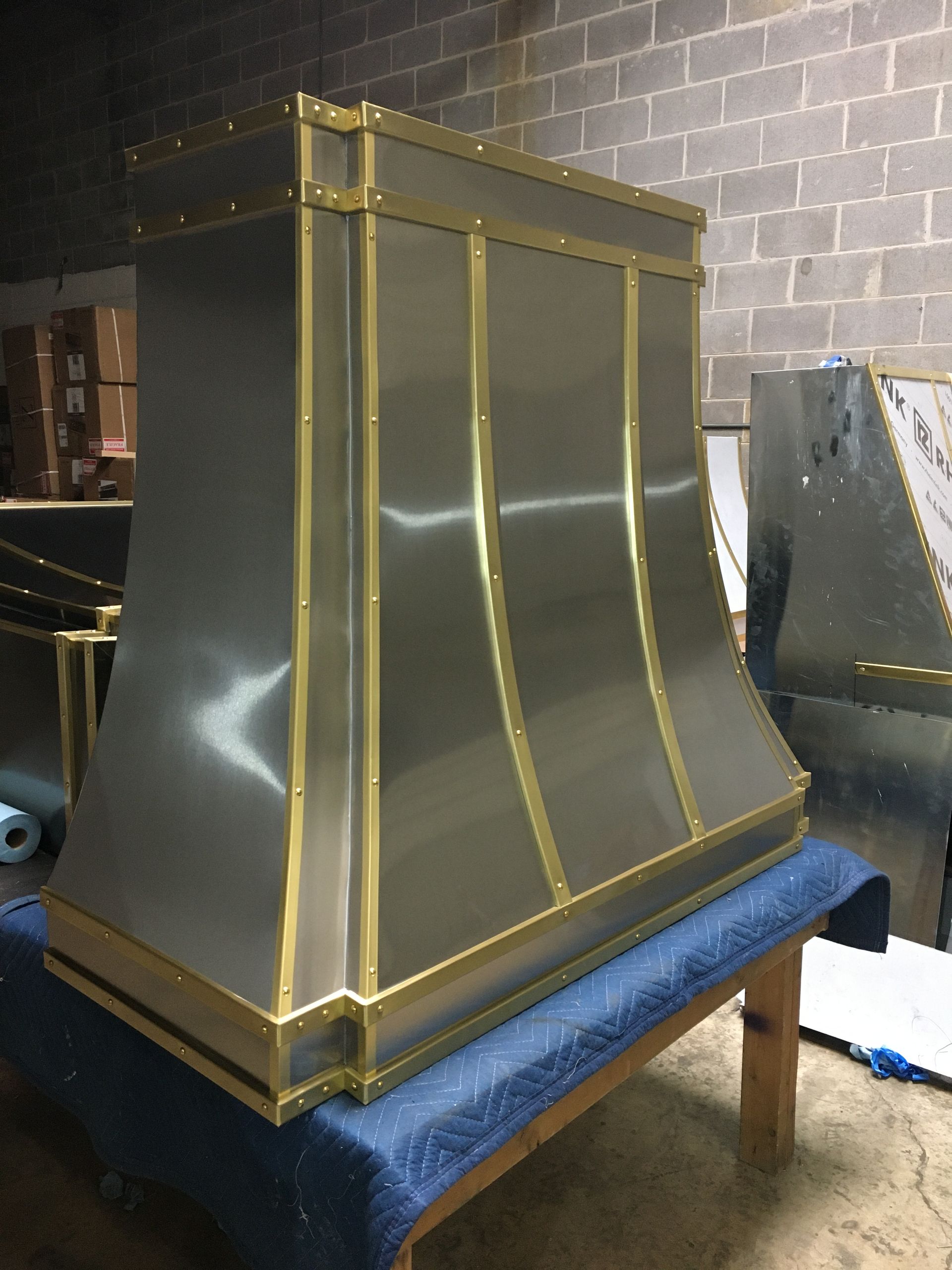 A stainless steel hood with brass trim is sitting on a wooden bench.