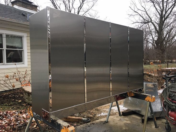 A large stainless steel cabinet is sitting on a clamp in front of a house.