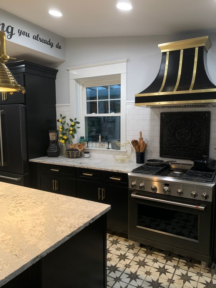 A kitchen with black cabinets , a stove , a refrigerator , and a window.