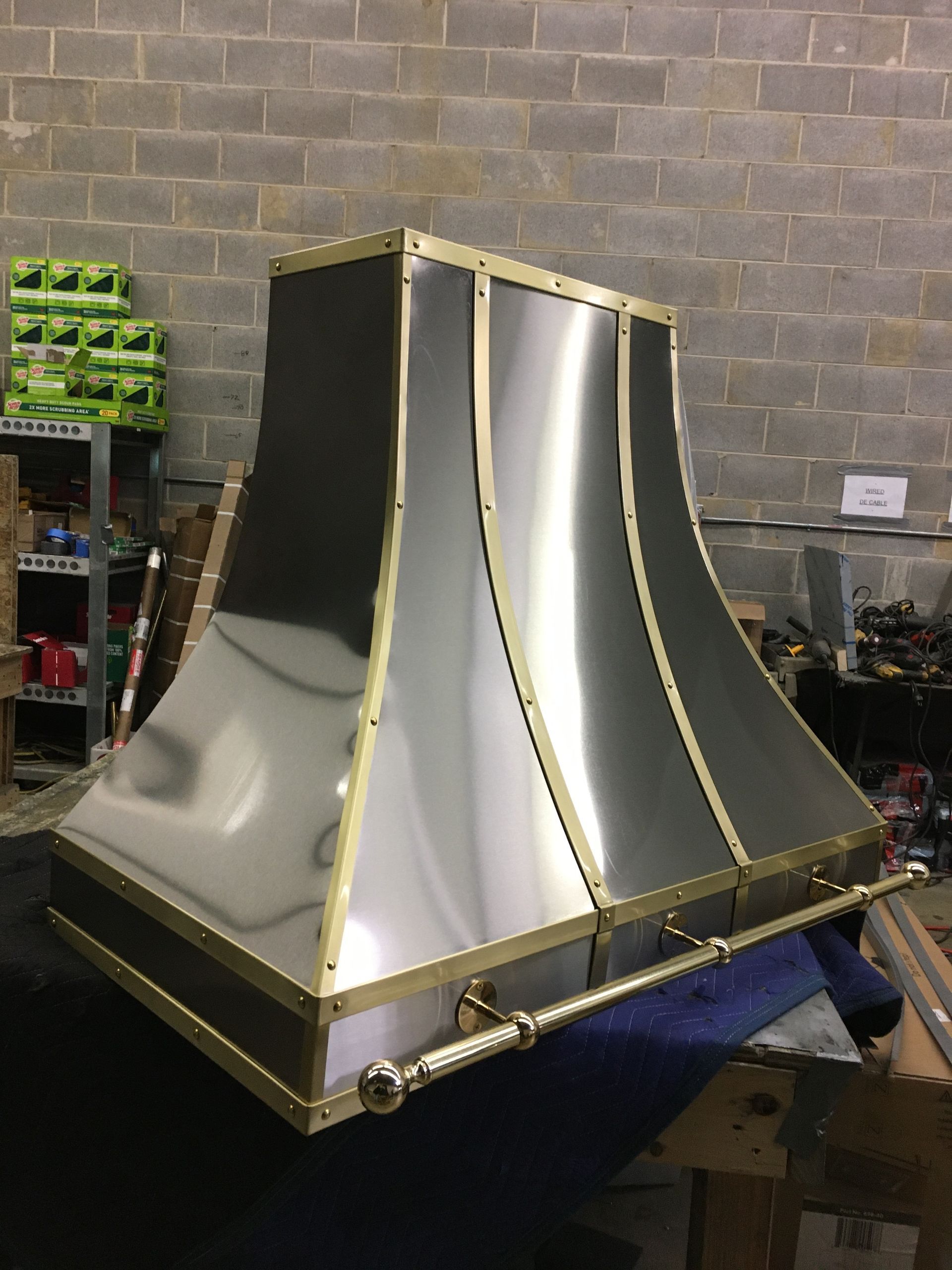 A stainless steel hood with brass trim is sitting in front of a brick wall.