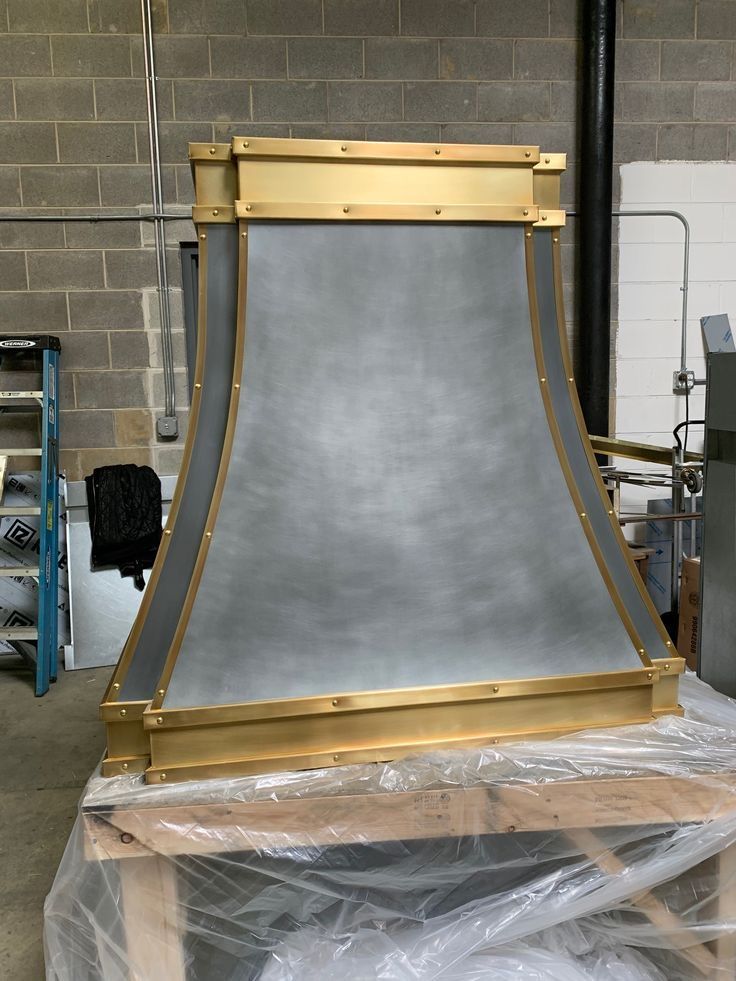 A metal hood with brass trim is sitting on top of a wooden table.