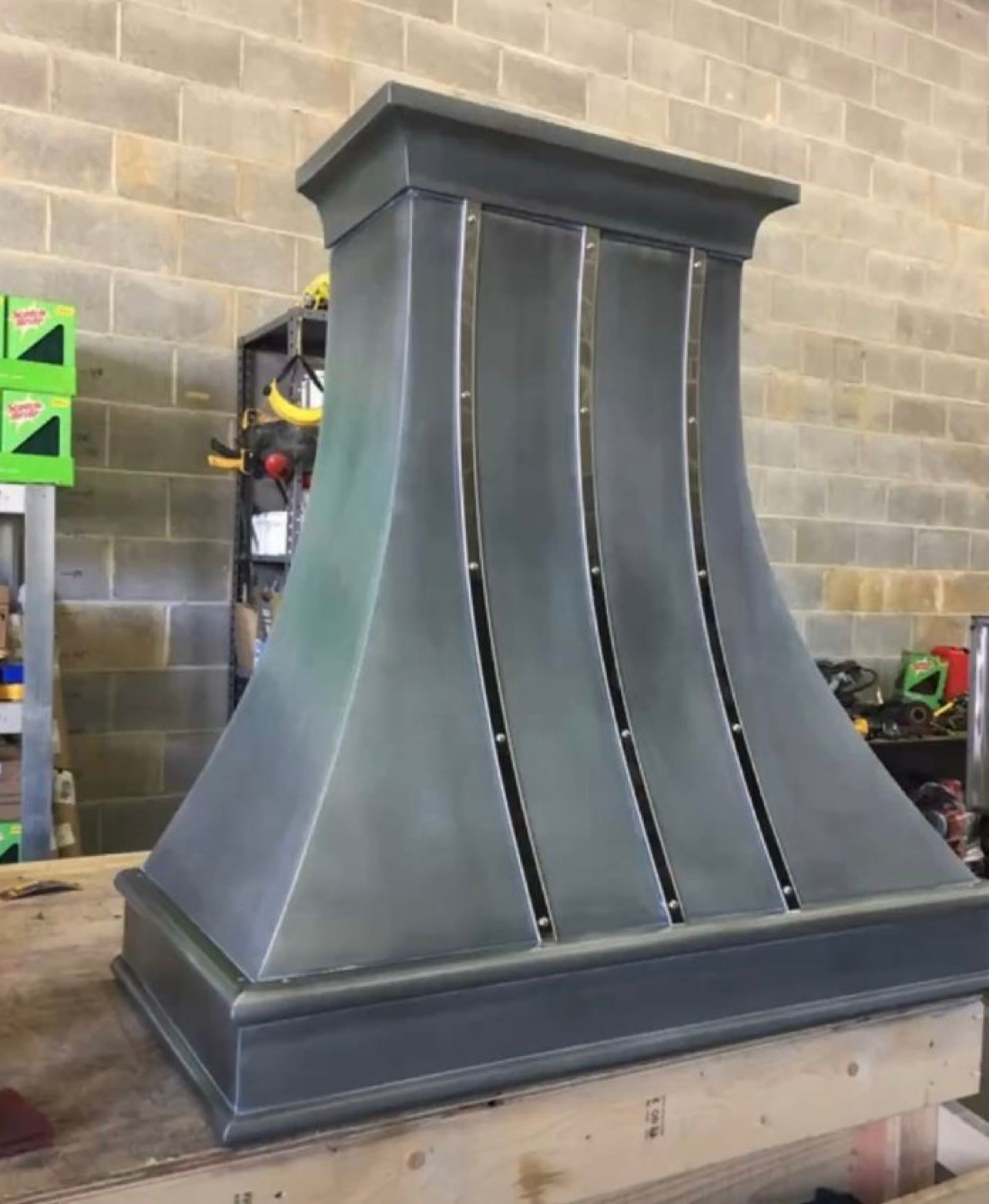 A metal hood is sitting on a wooden table in front of a brick wall