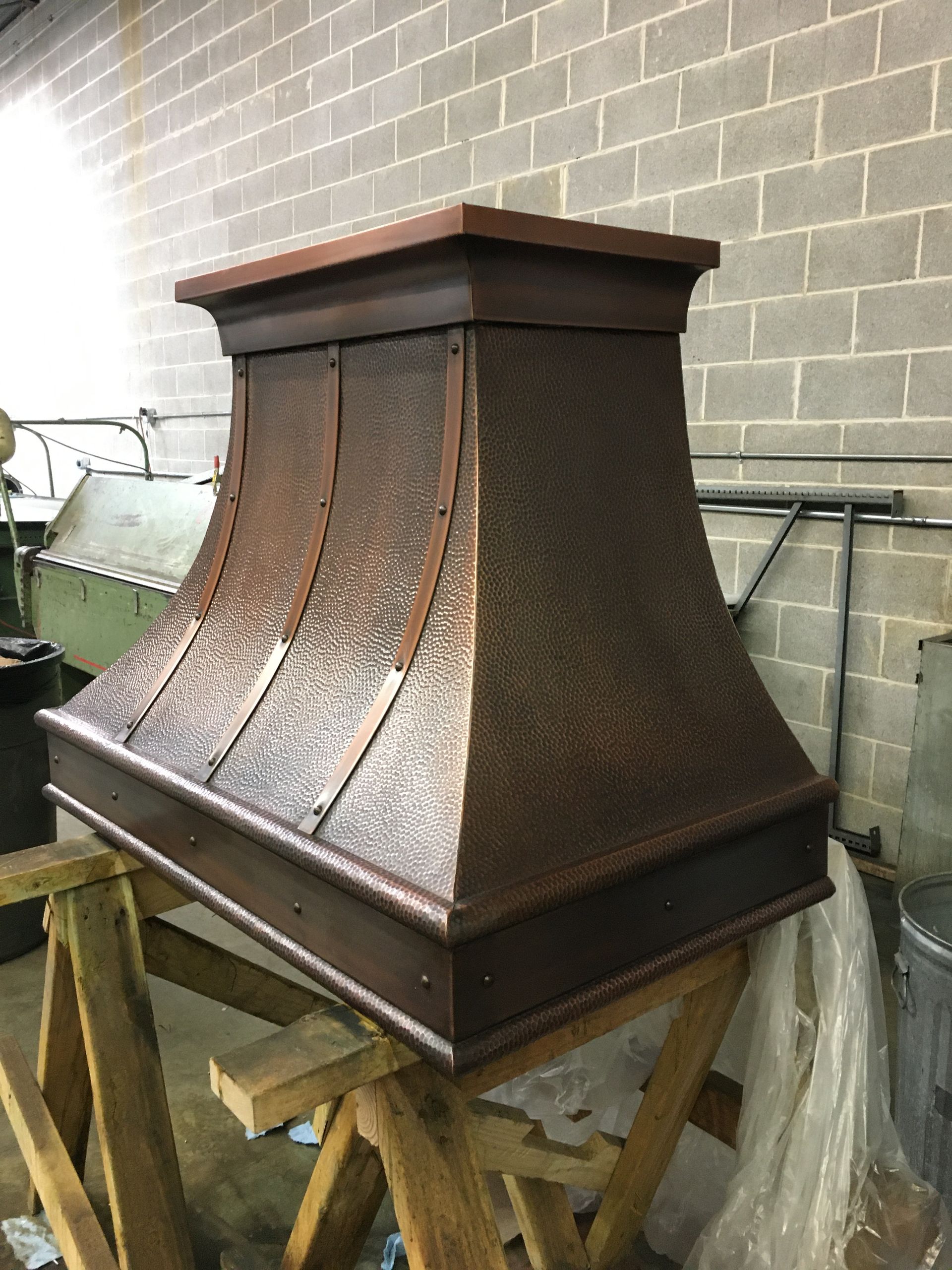 A copper hood is sitting on a wooden table in front of a brick wall.