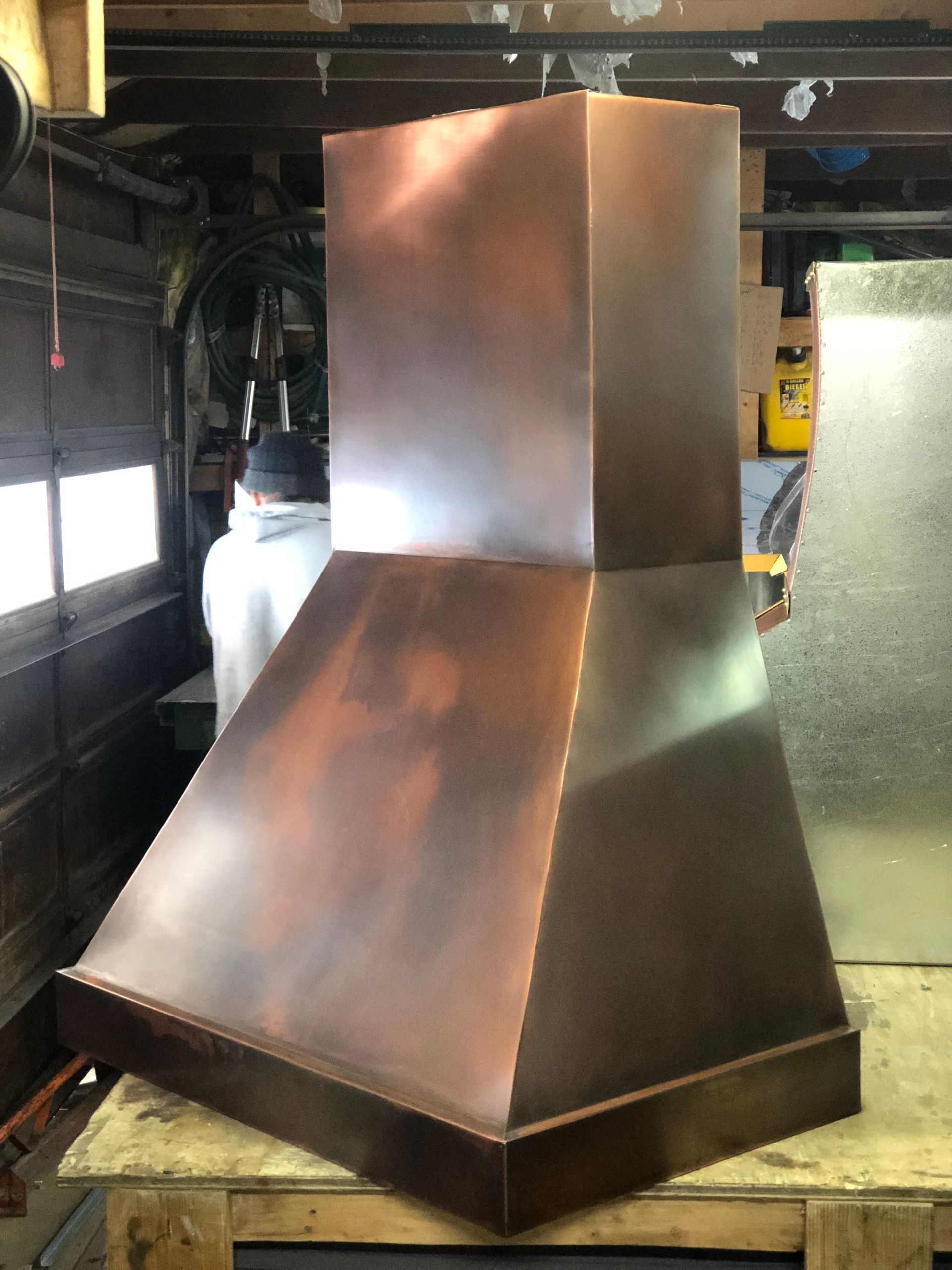 A copper hood is sitting on a wooden table in a garage.