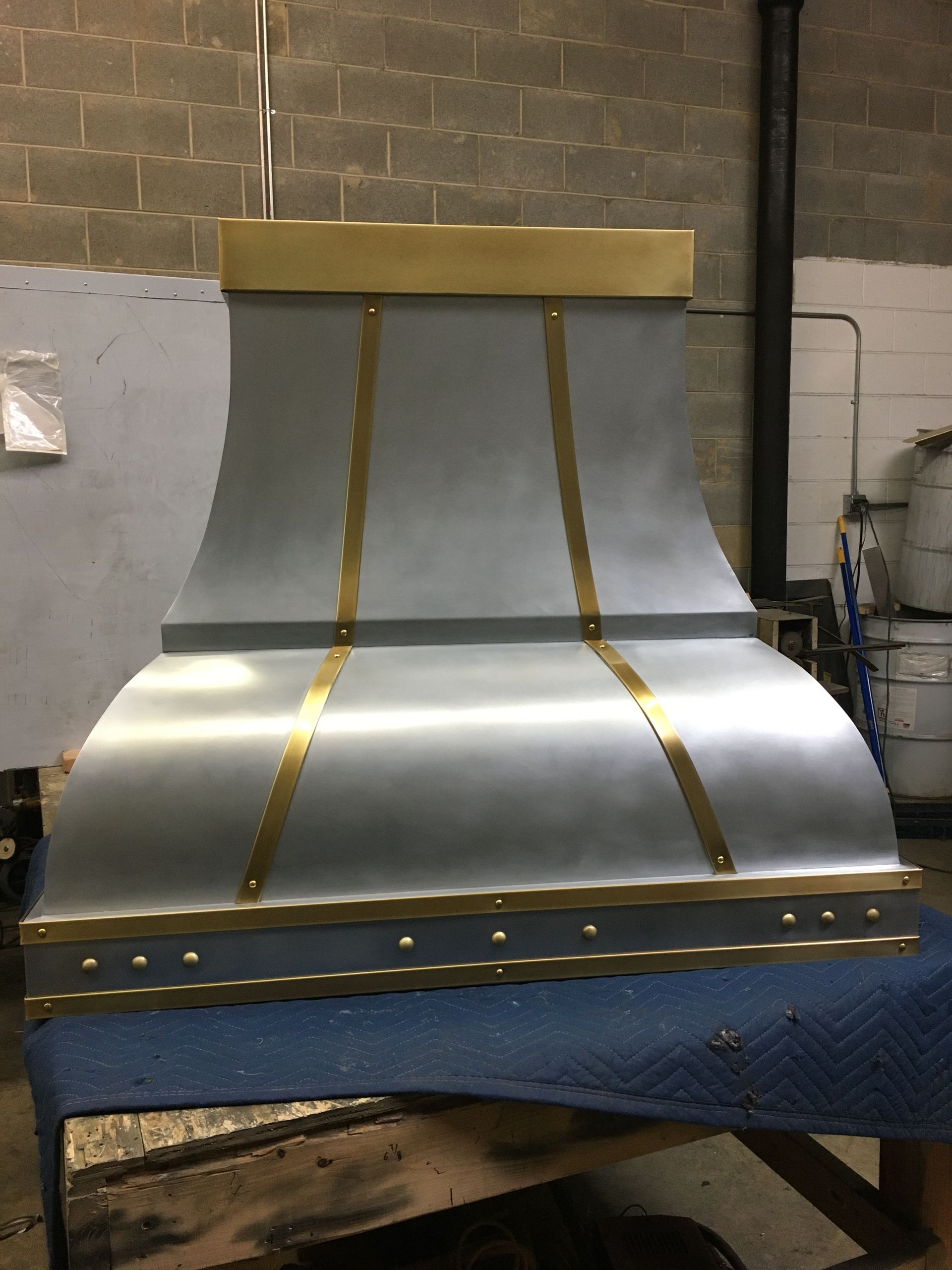 A stainless steel hood with brass trim sits on a table