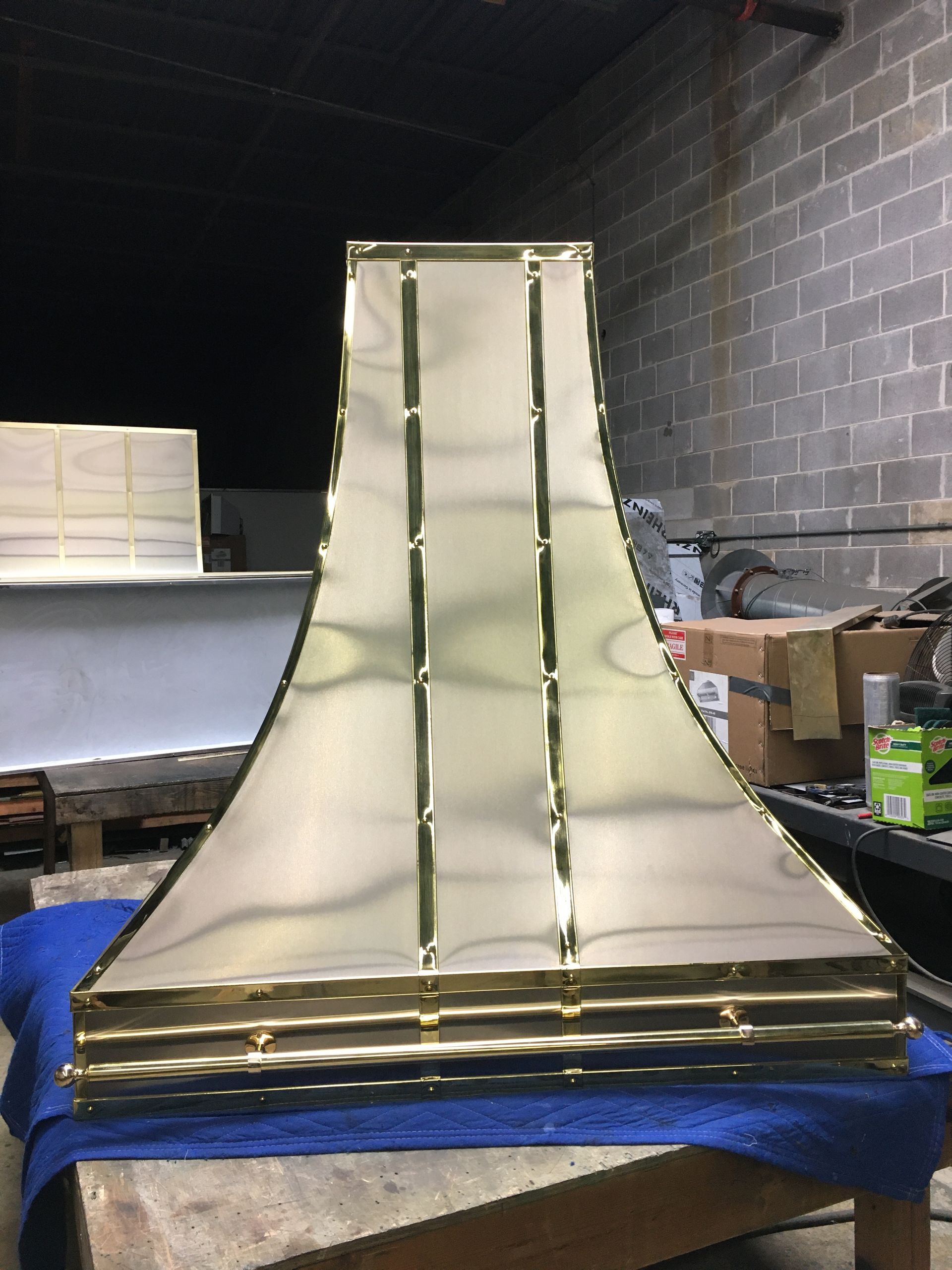 A large brass object is sitting on a table in front of a brick wall.