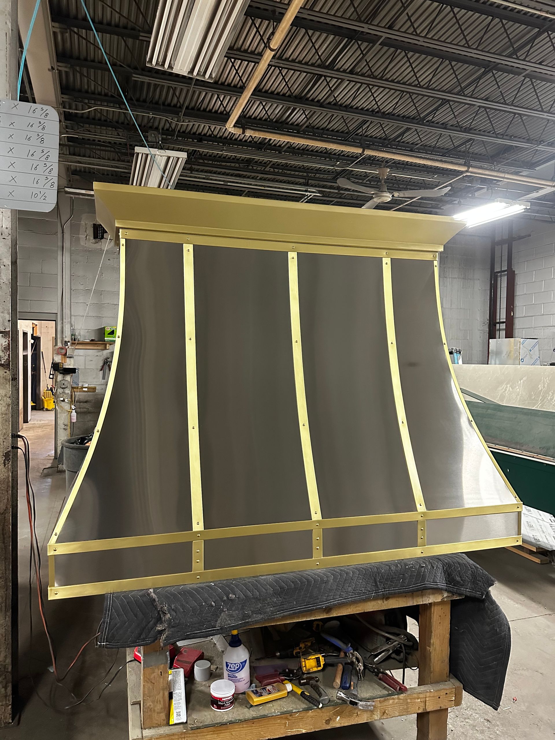 A stainless steel hood is sitting on top of a wooden table in a warehouse.