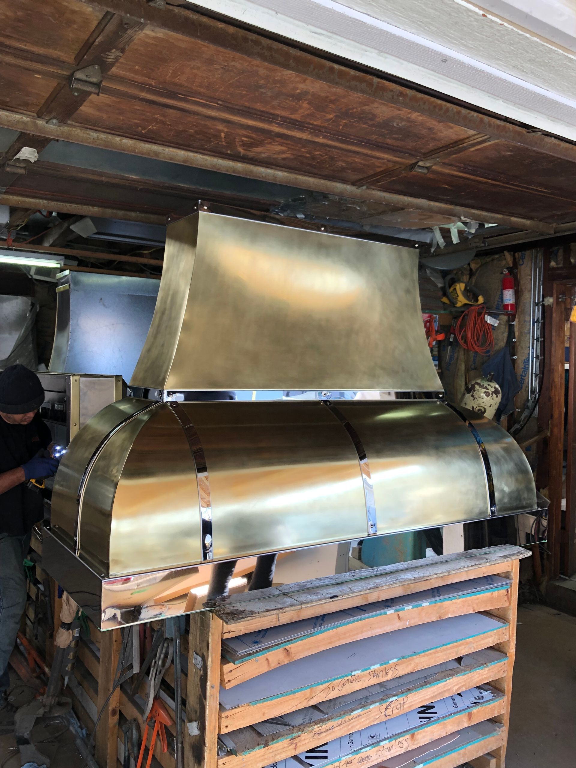 A man is working on a brass hood in a garage.