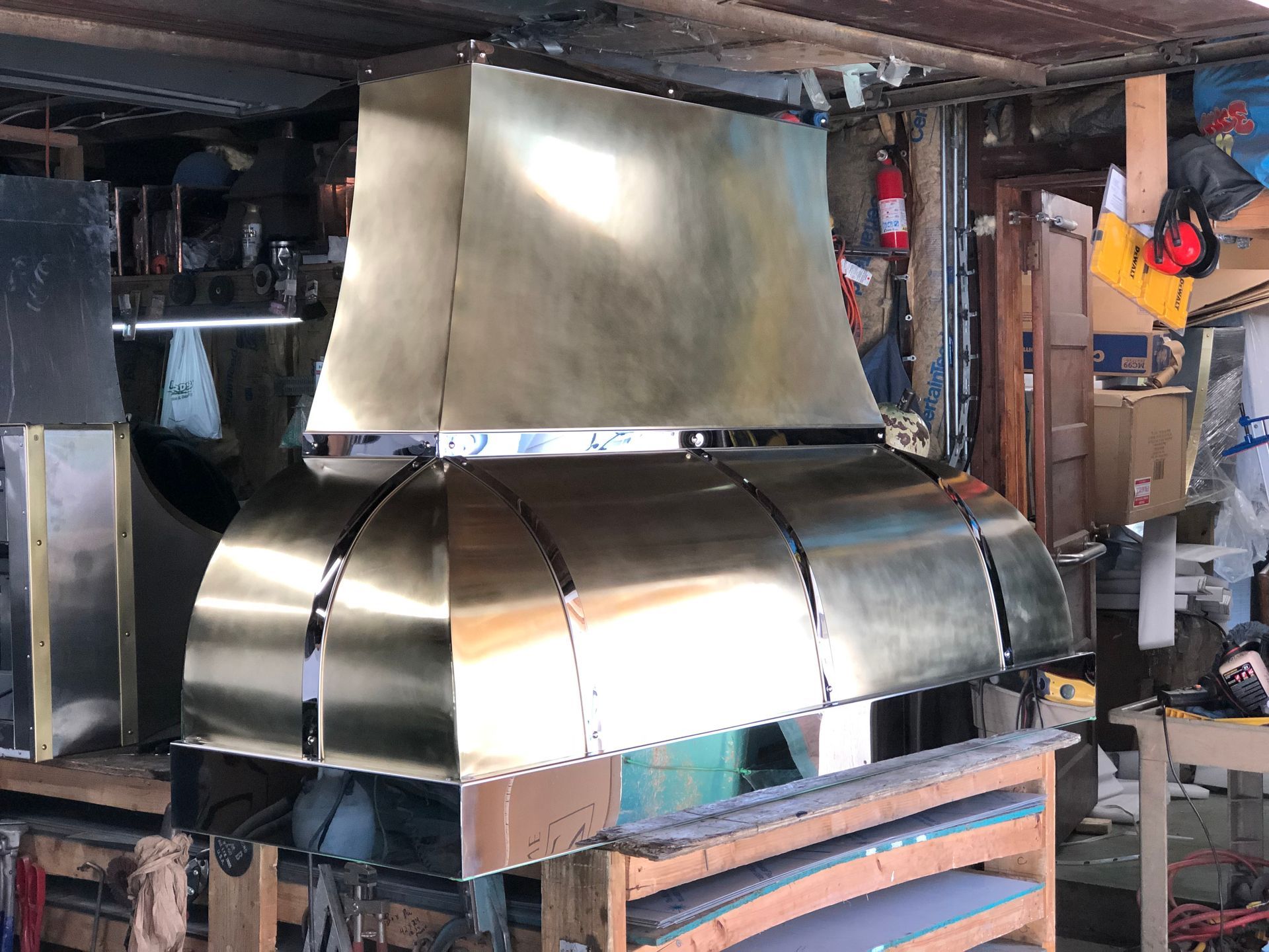 A brass hood is sitting on top of a wooden table in a garage.