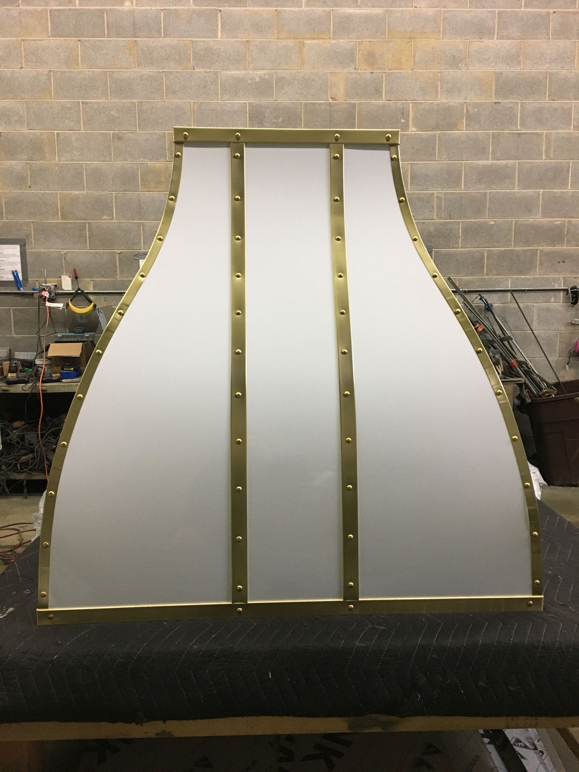 A stainless steel hood with brass trim is sitting on a table in front of a brick wall.