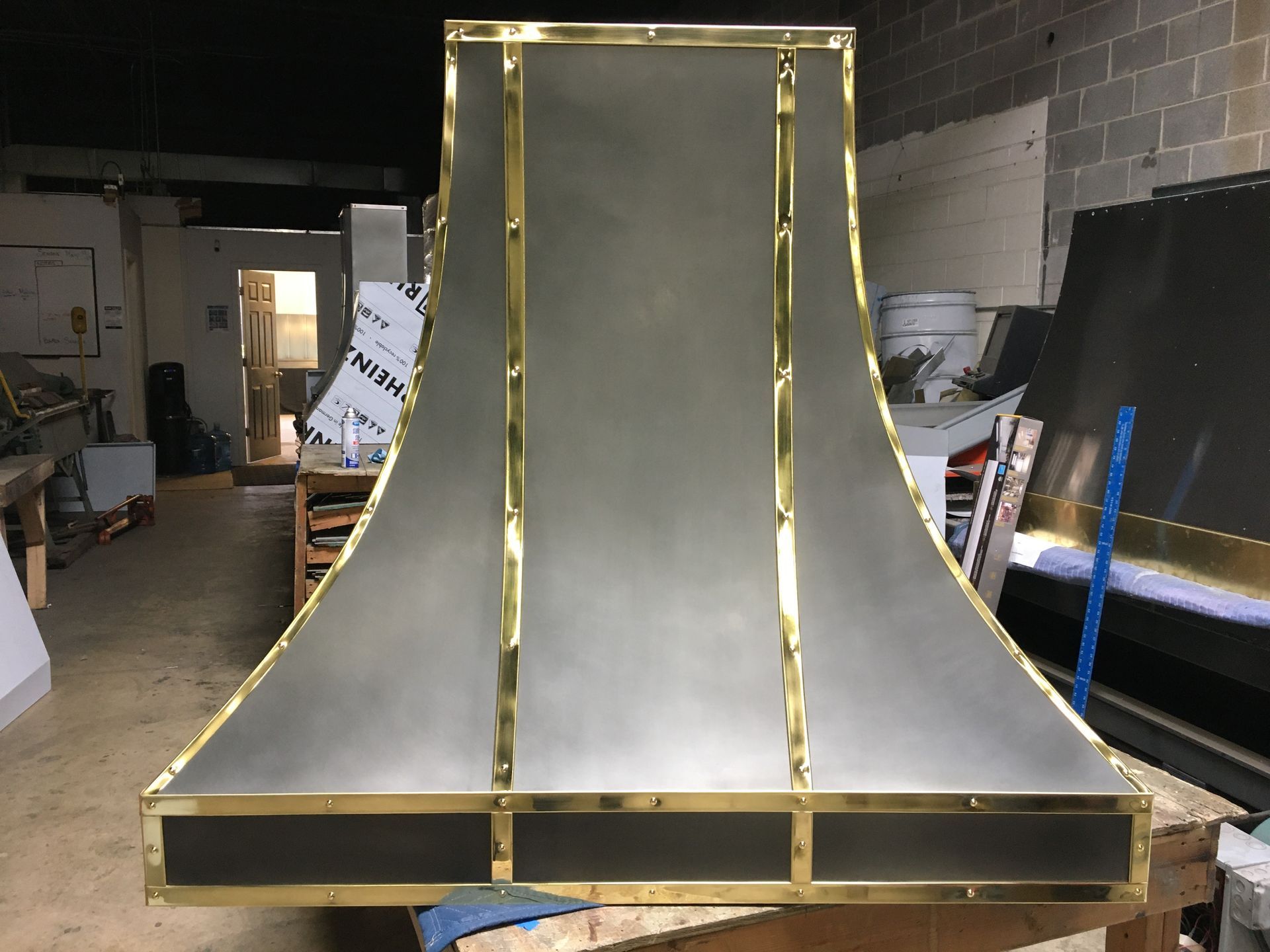 A stainless steel hood with brass trim is sitting on a wooden table in a room.