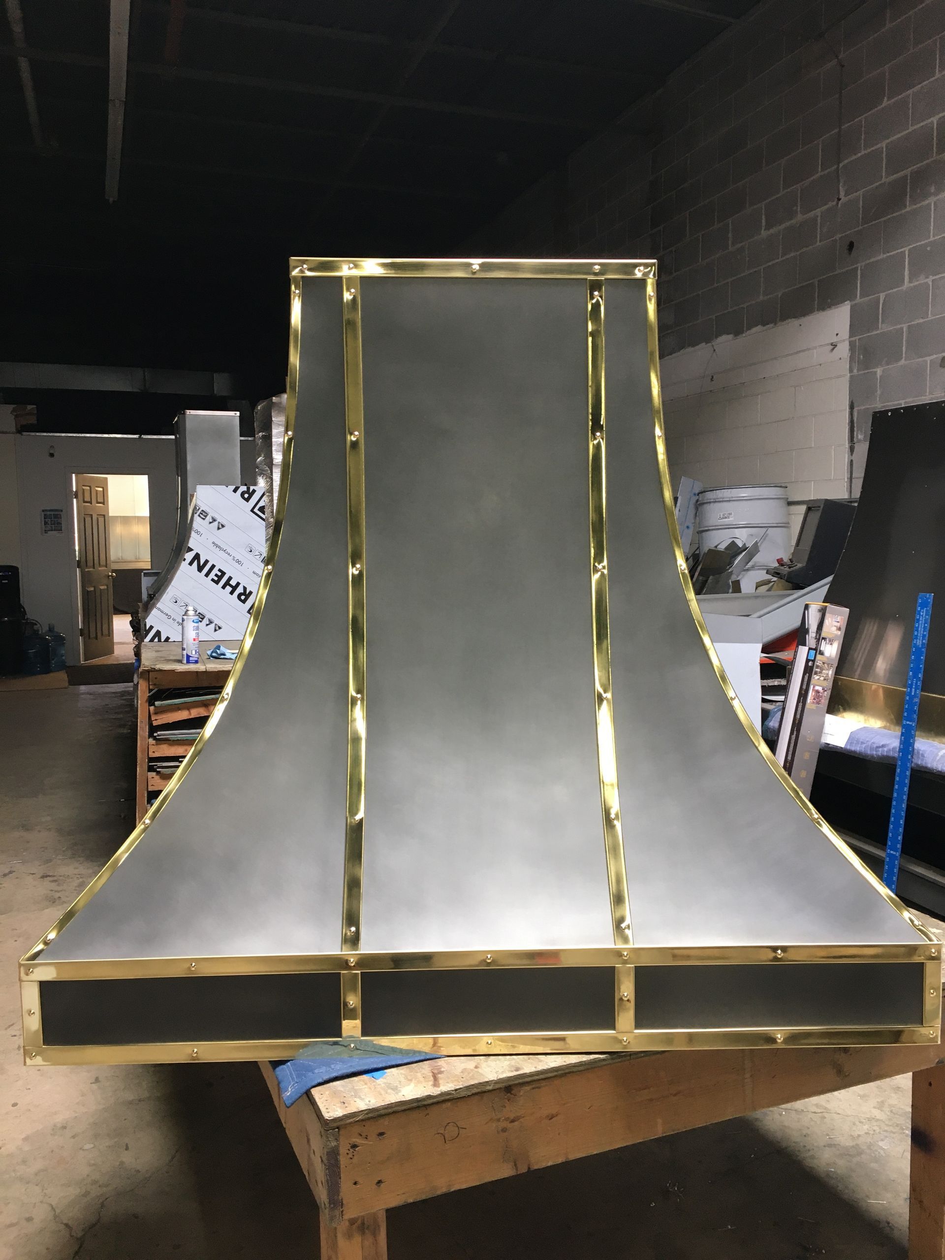 A stainless steel hood with brass trim sits on a wooden table