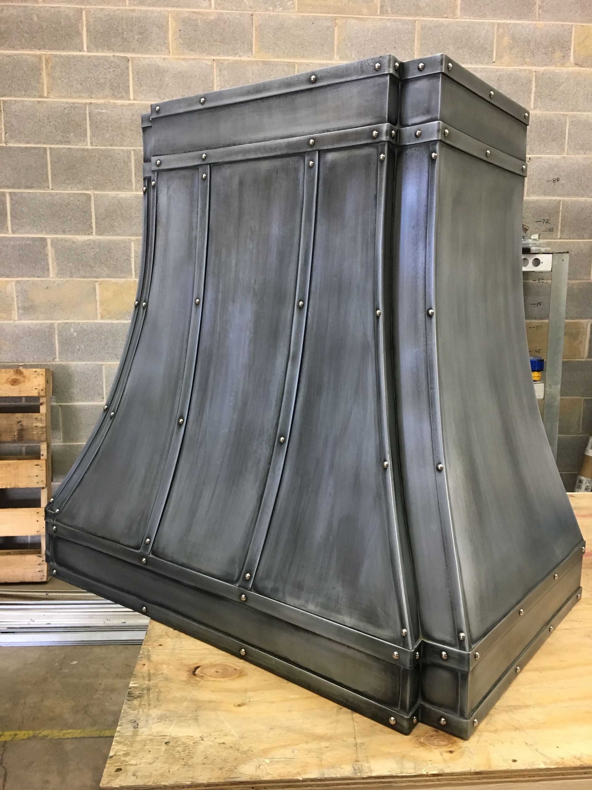 A metal hood is sitting on a wooden table in front of a brick wall.