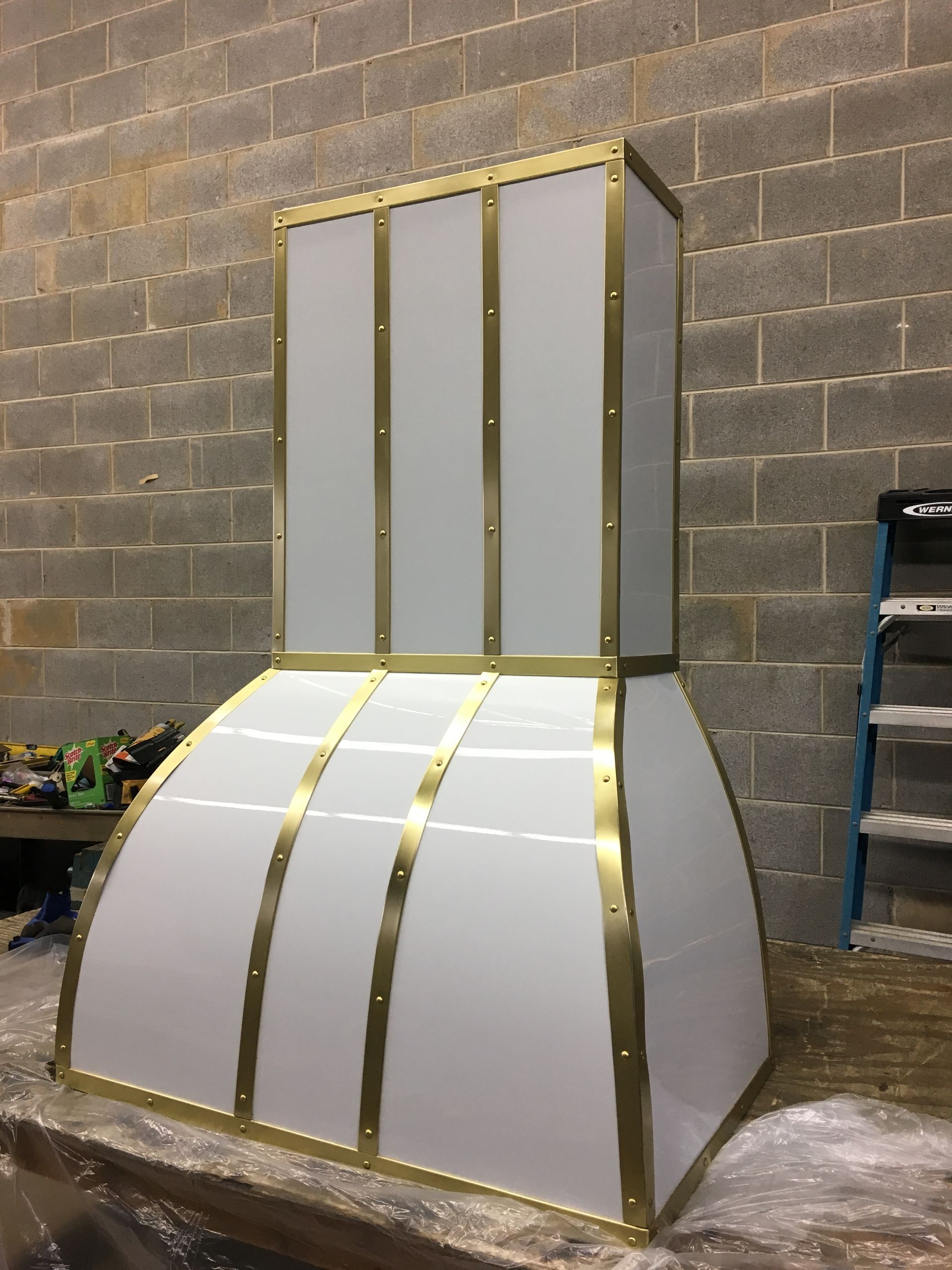 A white and gold hood is sitting on a table in front of a brick wall.