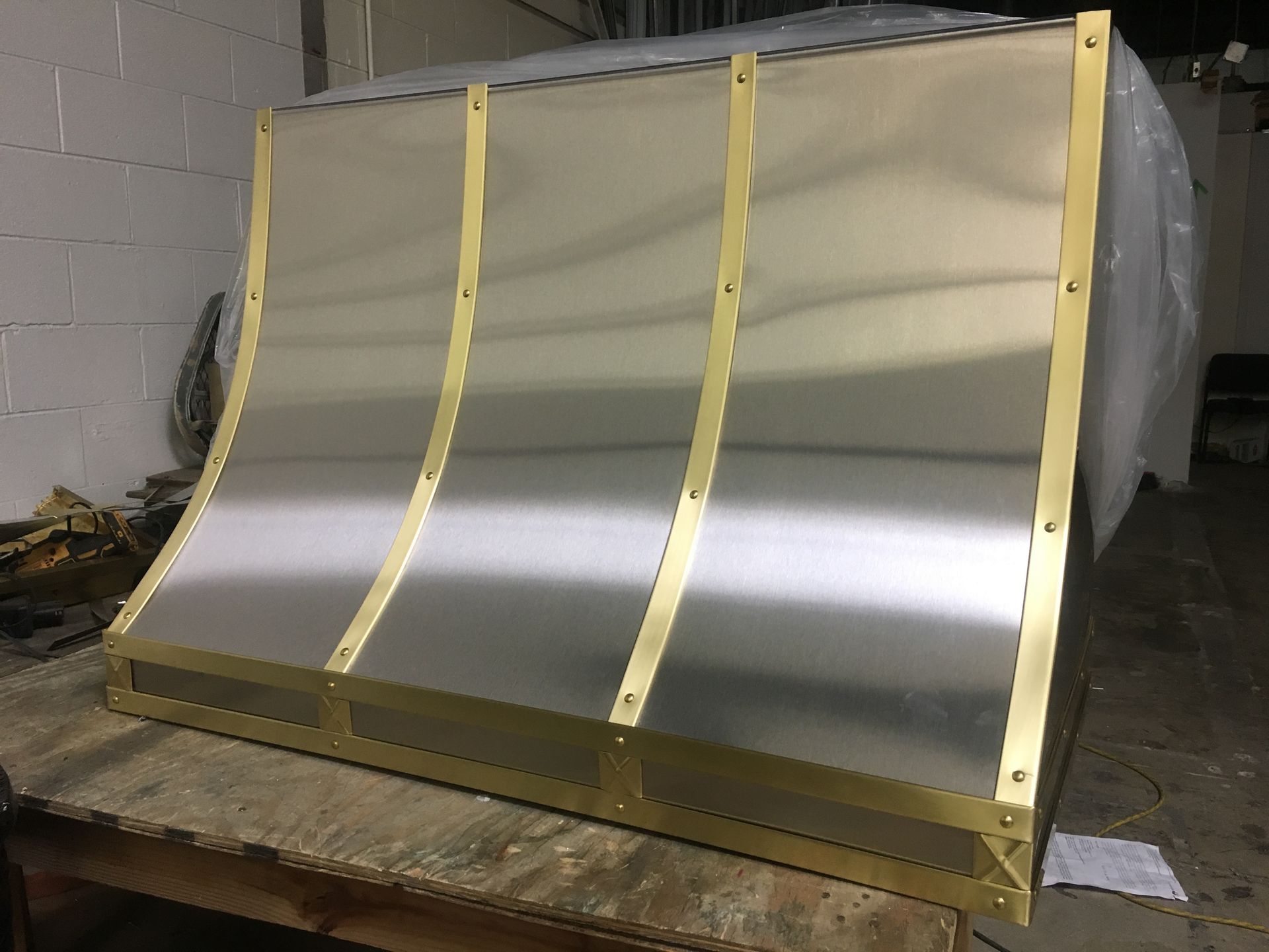 A stainless steel hood with brass trim is sitting on a wooden table.