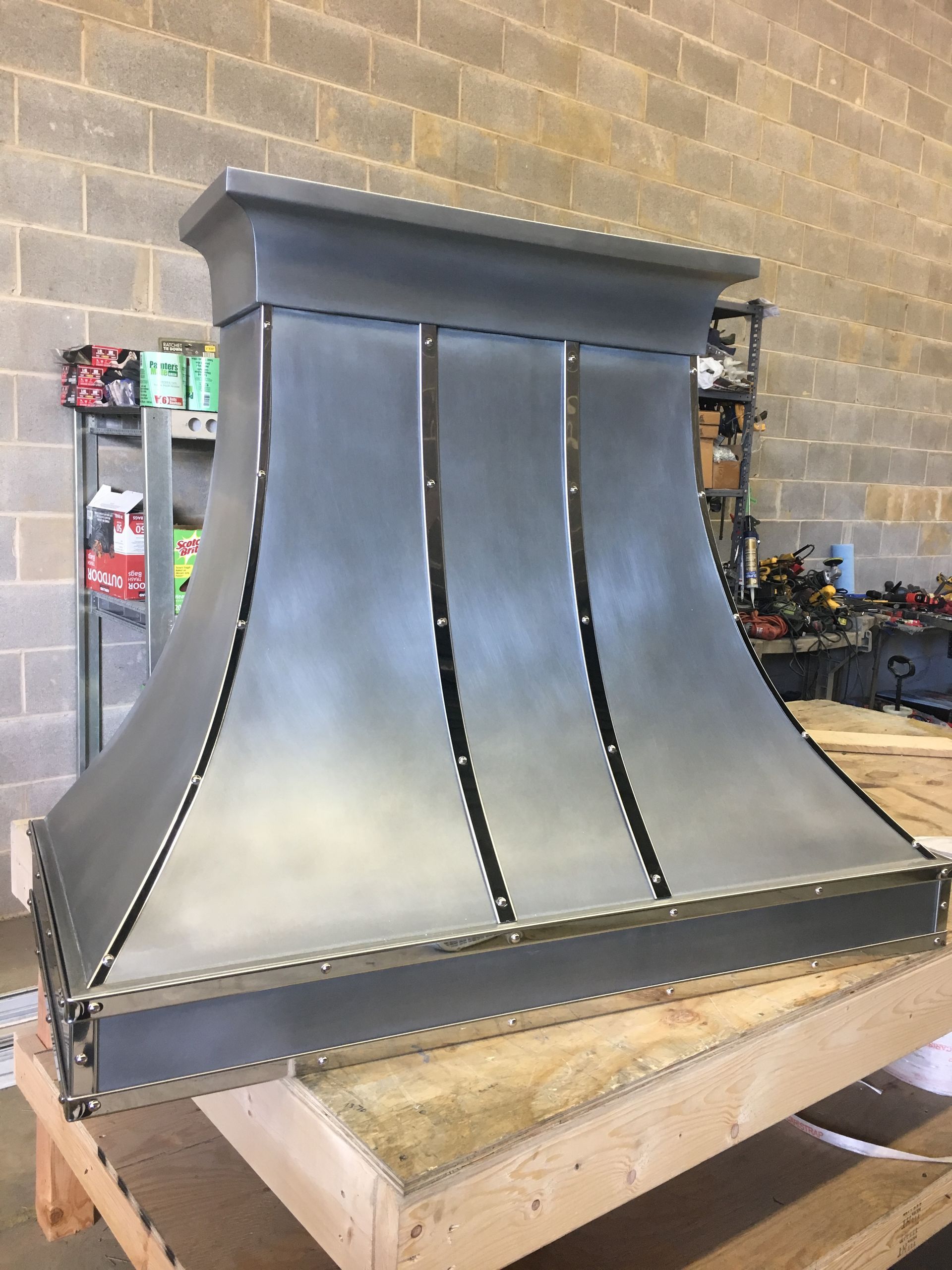 A metal hood is sitting on a wooden table in front of a brick wall.