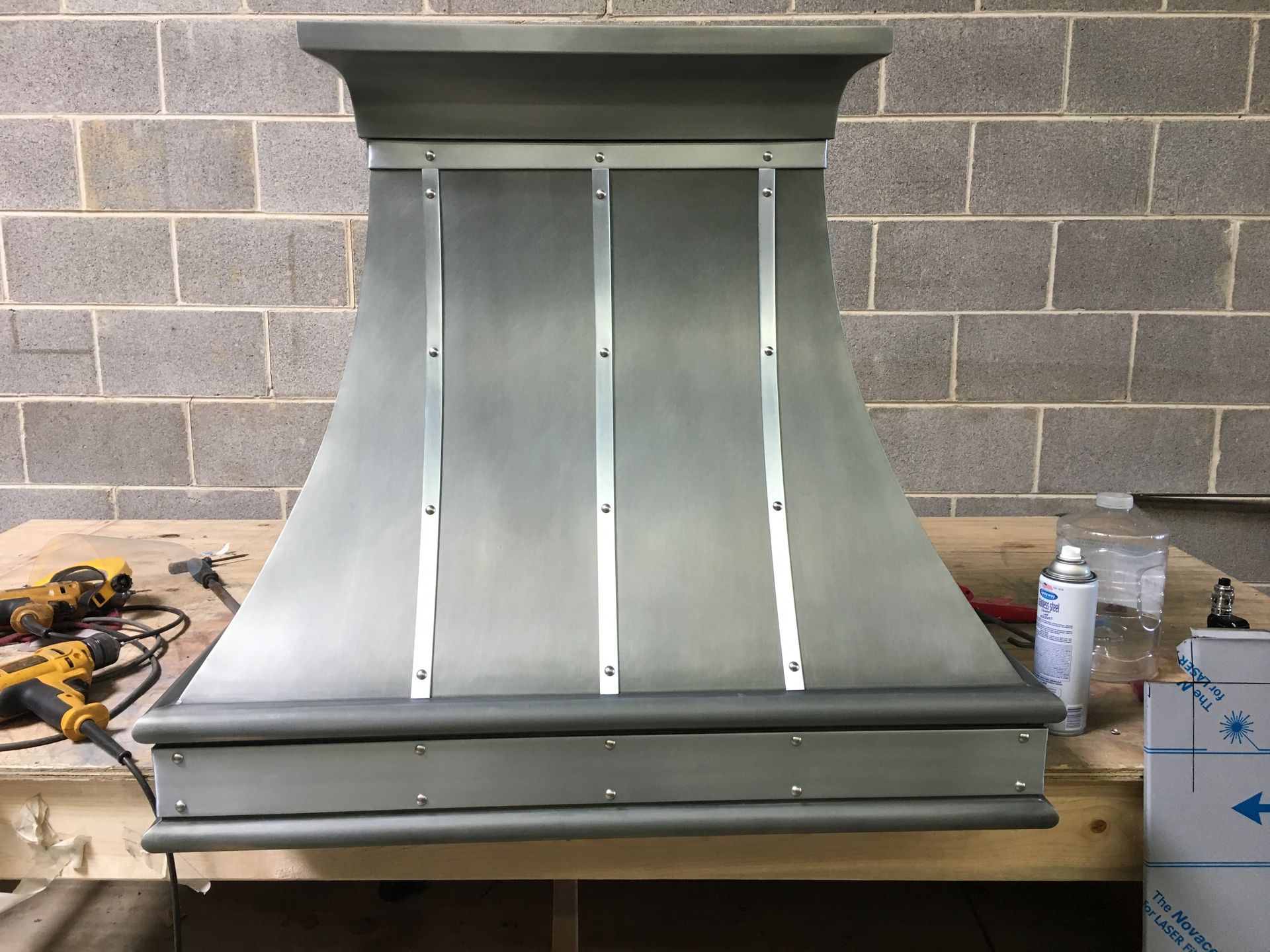 A stainless steel hood is sitting on a wooden table in front of a brick wall