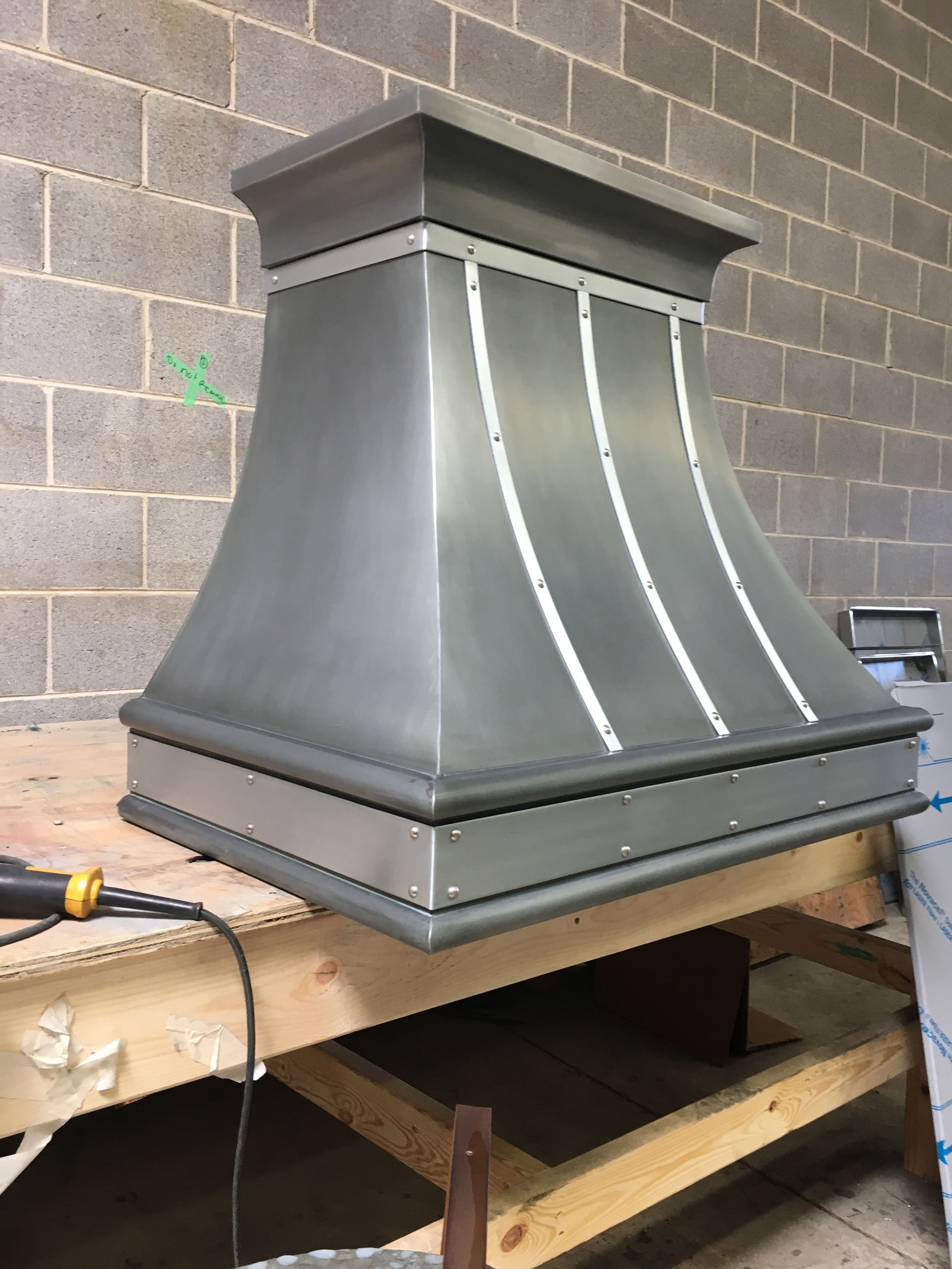 A metal hood is sitting on a wooden table in front of a brick wall.