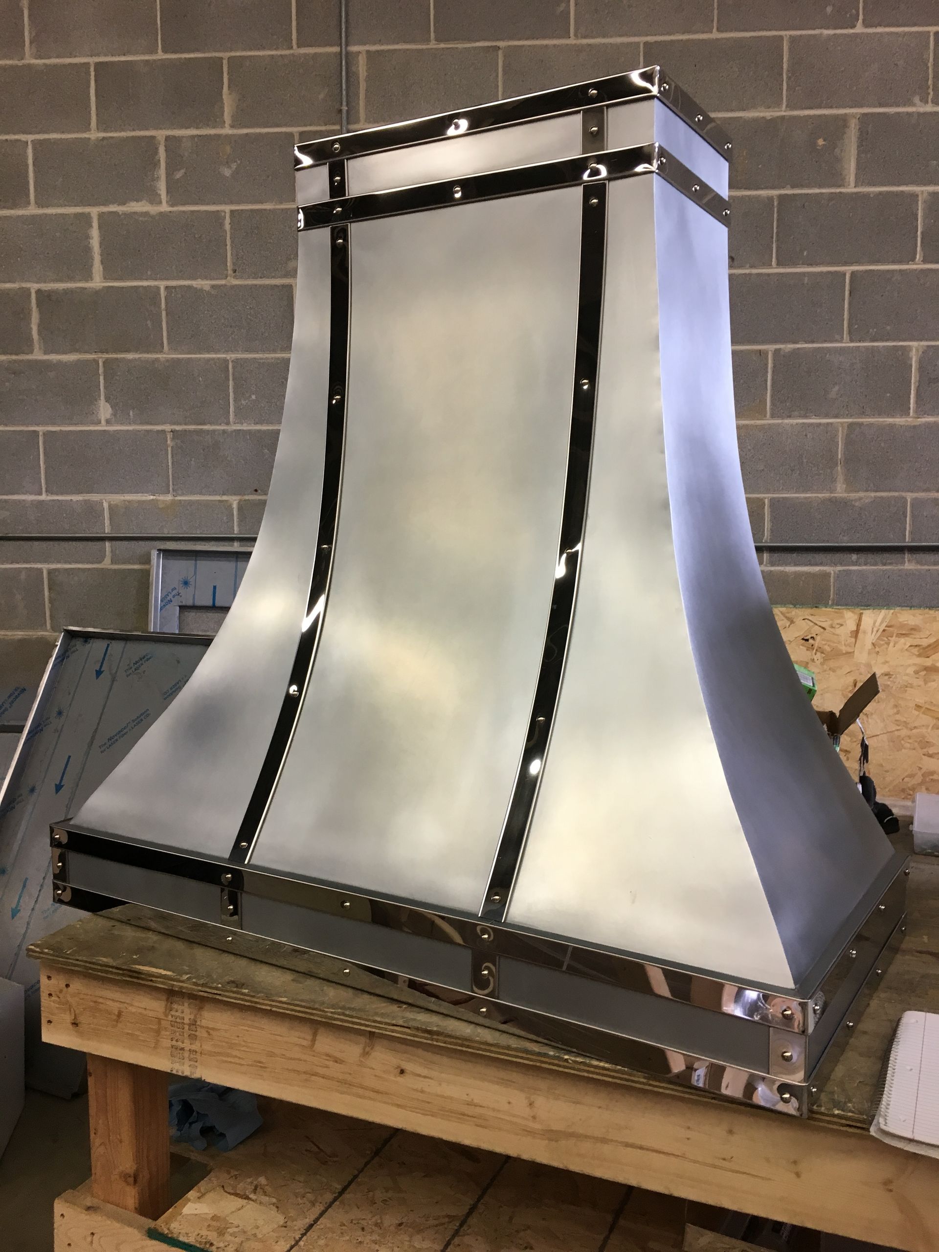 A stainless steel hood is sitting on a wooden table in front of a brick wall