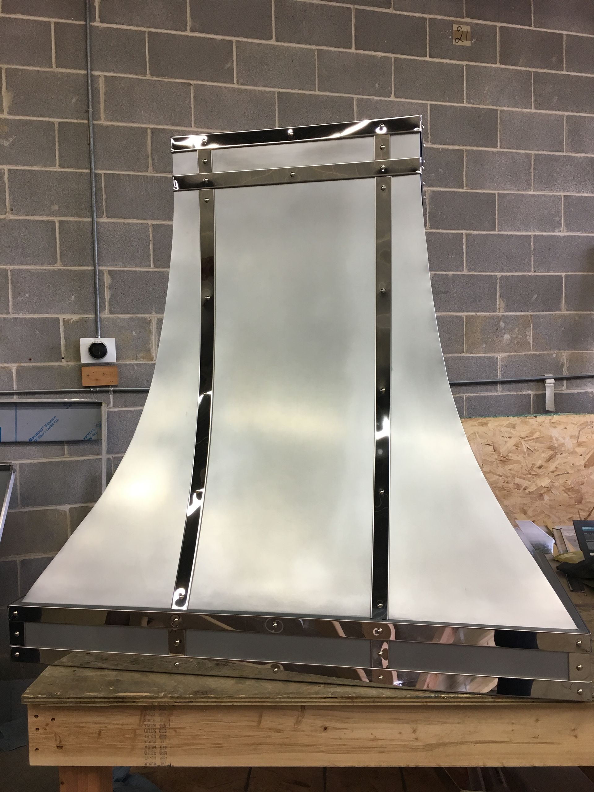 A stainless steel hood is sitting on a wooden table in front of a brick wall.