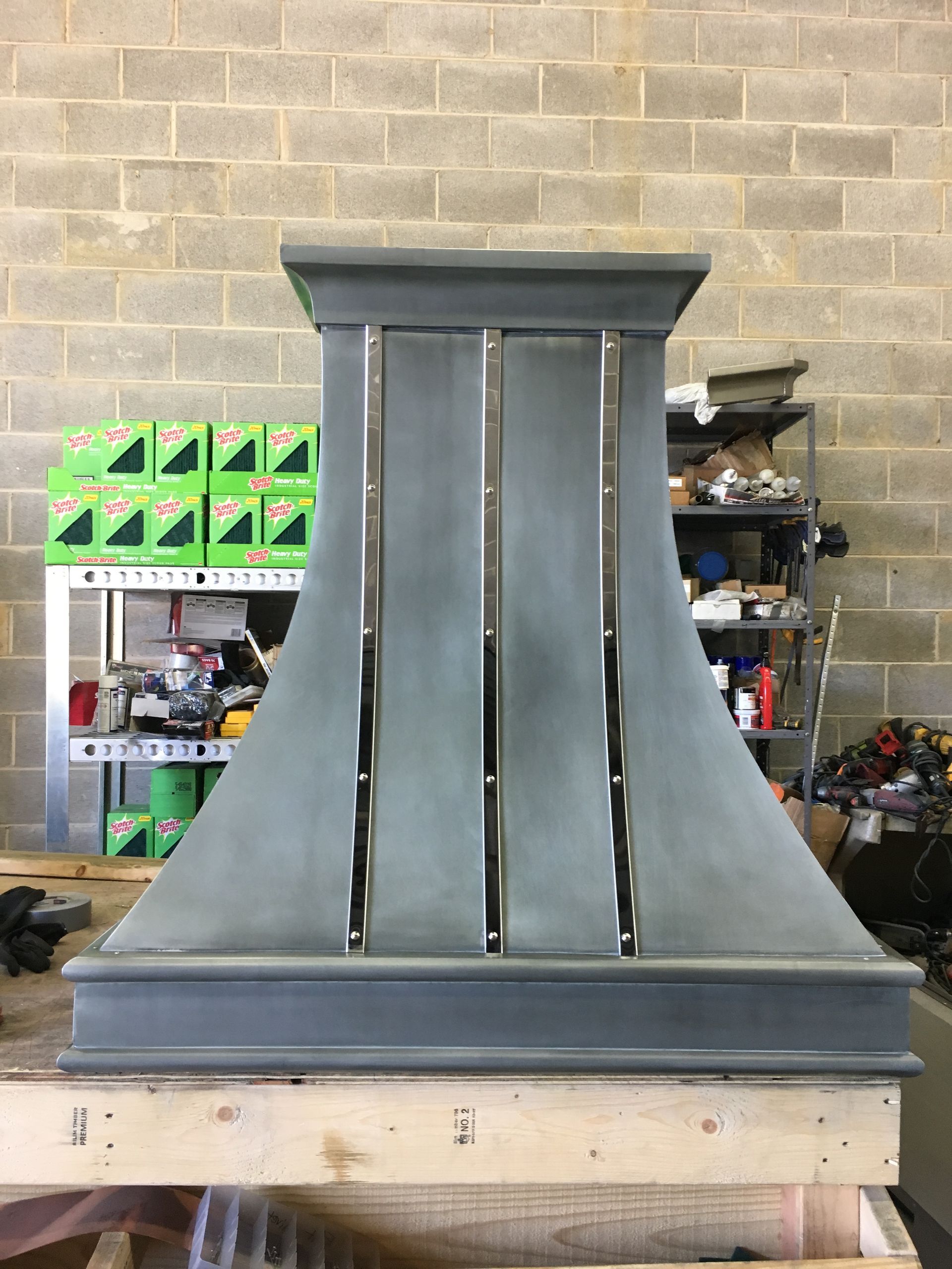 A metal hood is sitting on a wooden table in front of a brick wall.