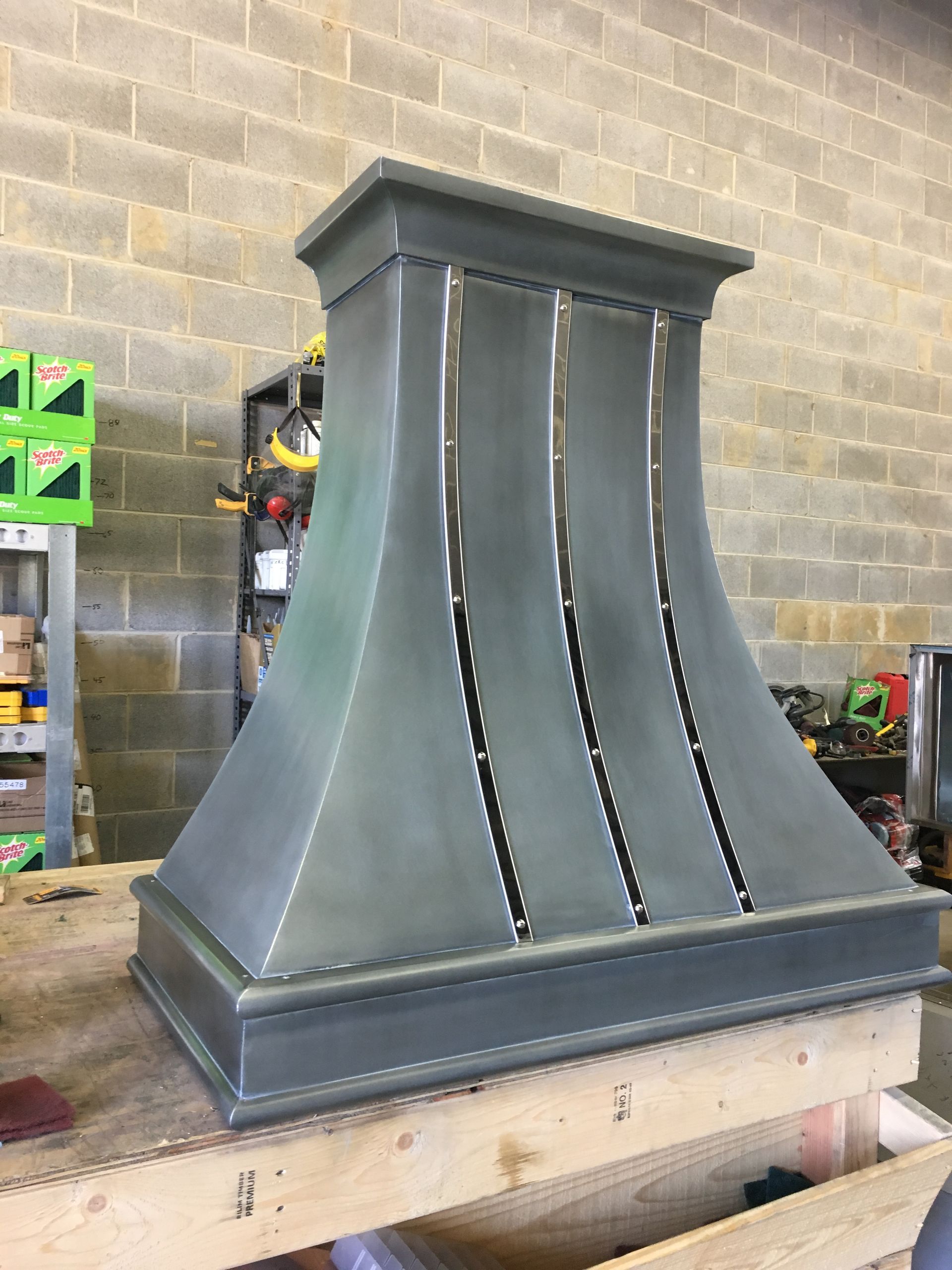 A metal hood is sitting on a wooden table in front of a brick wall.