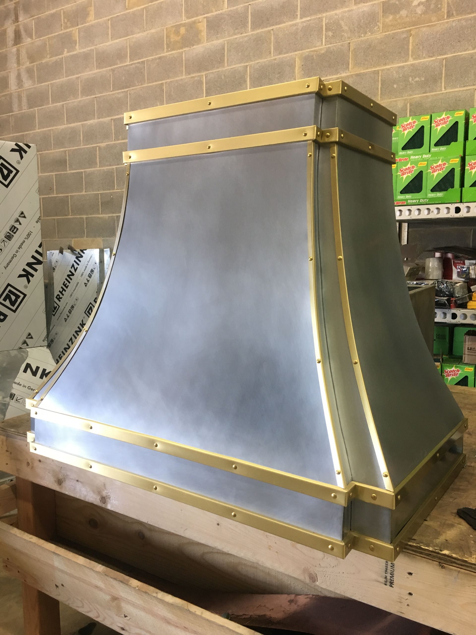 A stainless steel hood with brass trim is sitting on a wooden table.