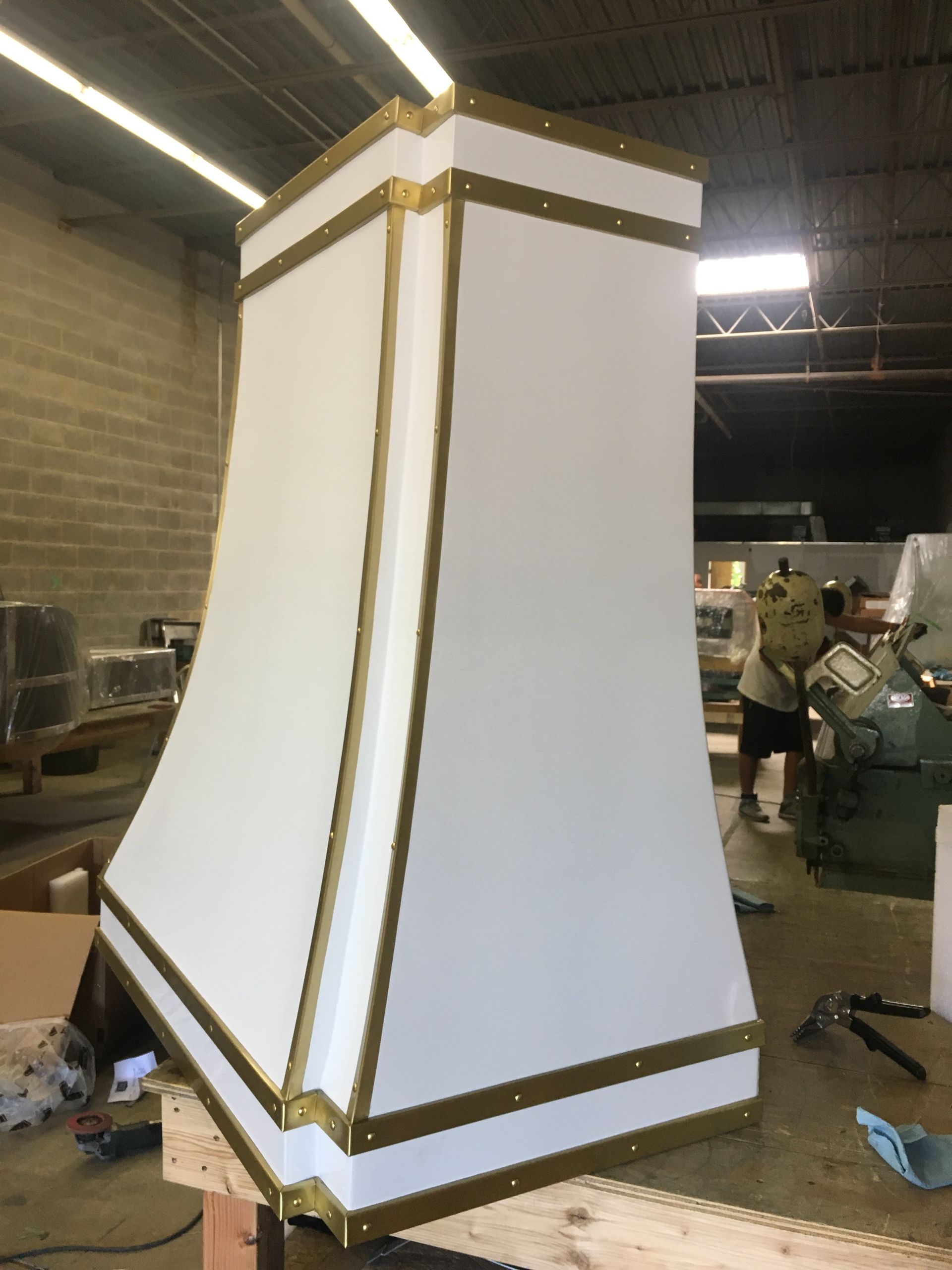 A white lamp shade with gold trim is sitting on a wooden table in a warehouse.