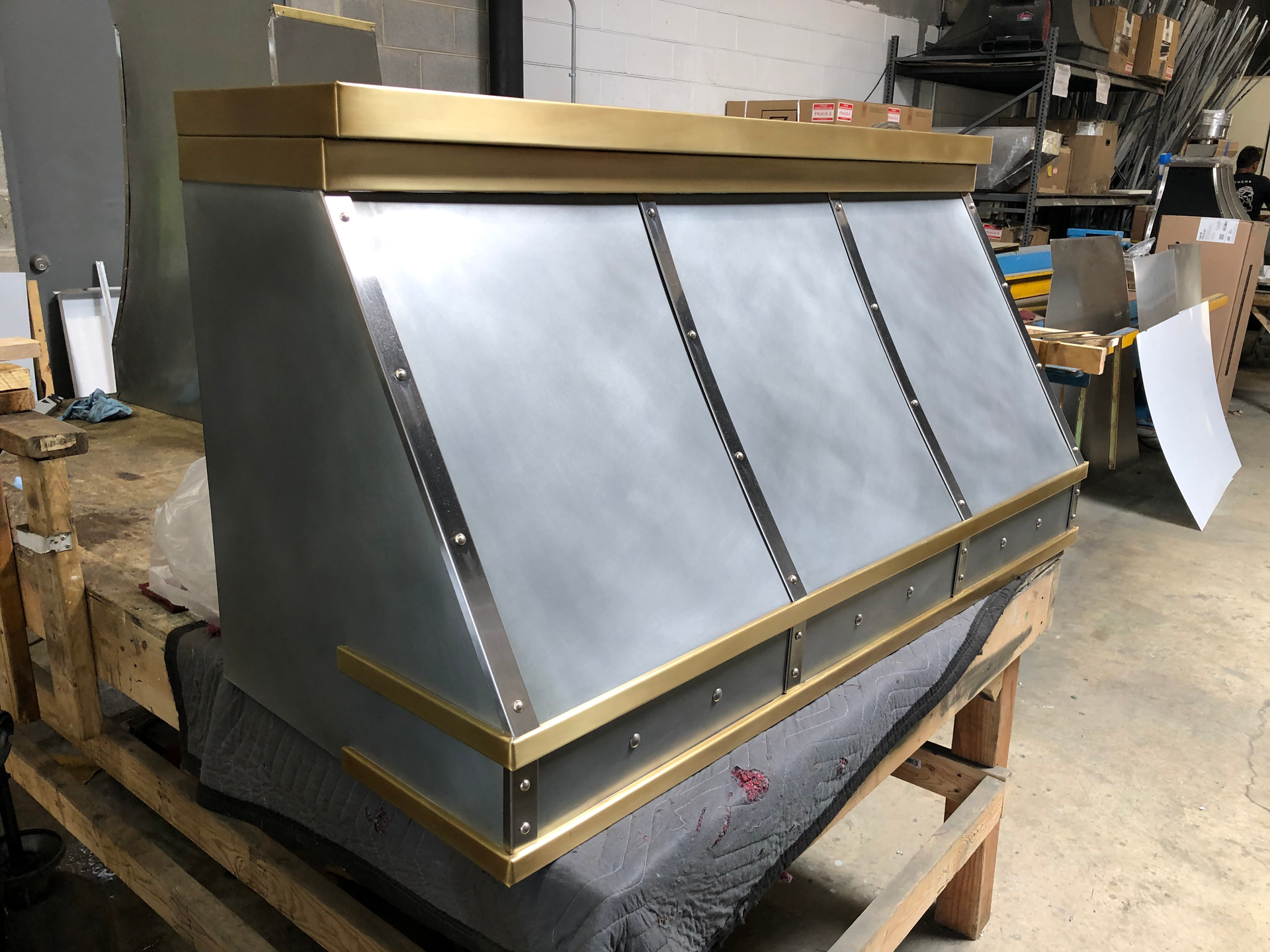 A metal hood with brass trim is sitting on top of a wooden pallet.