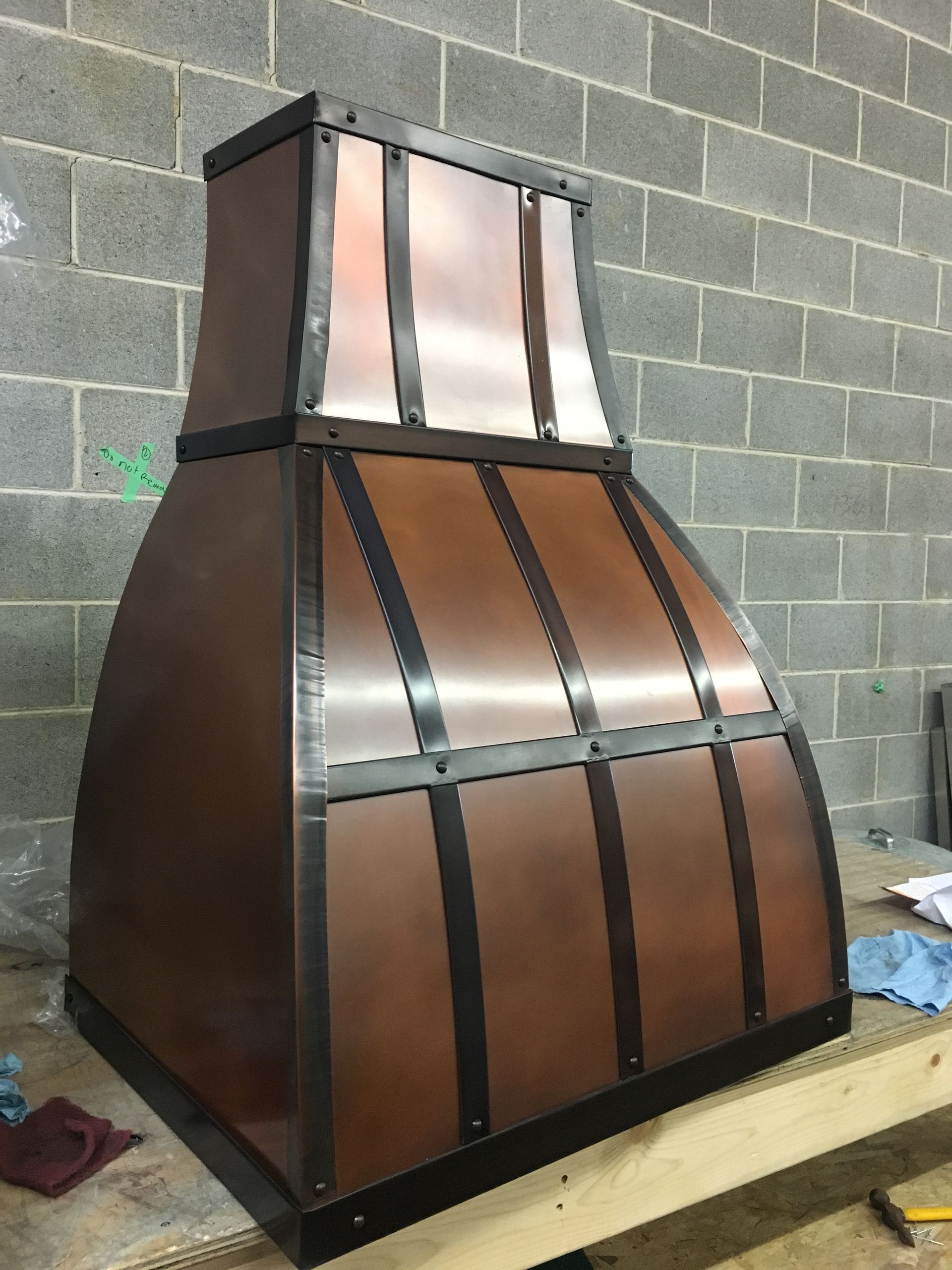 A copper hood is sitting on a wooden table in front of a brick wall.