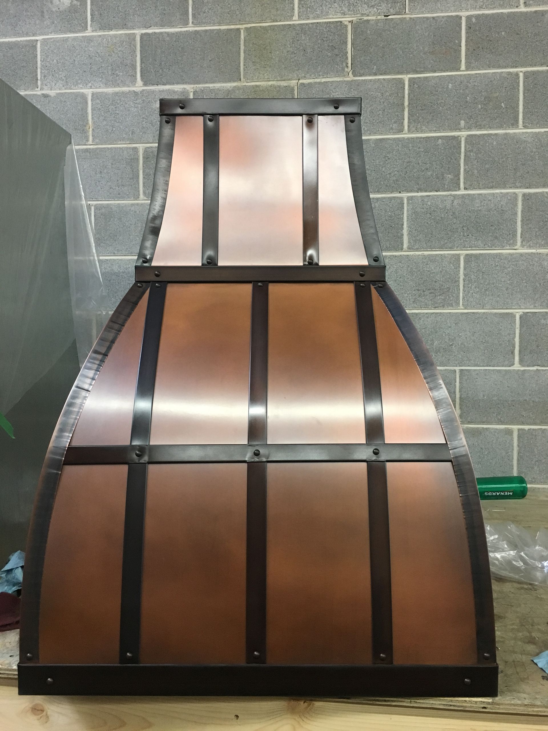 A copper hood is sitting on a wooden table in front of a brick wall