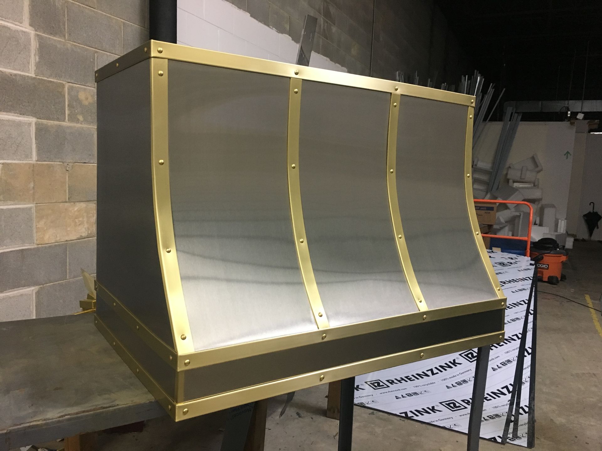 A stainless steel hood with brass trim is sitting on a table.