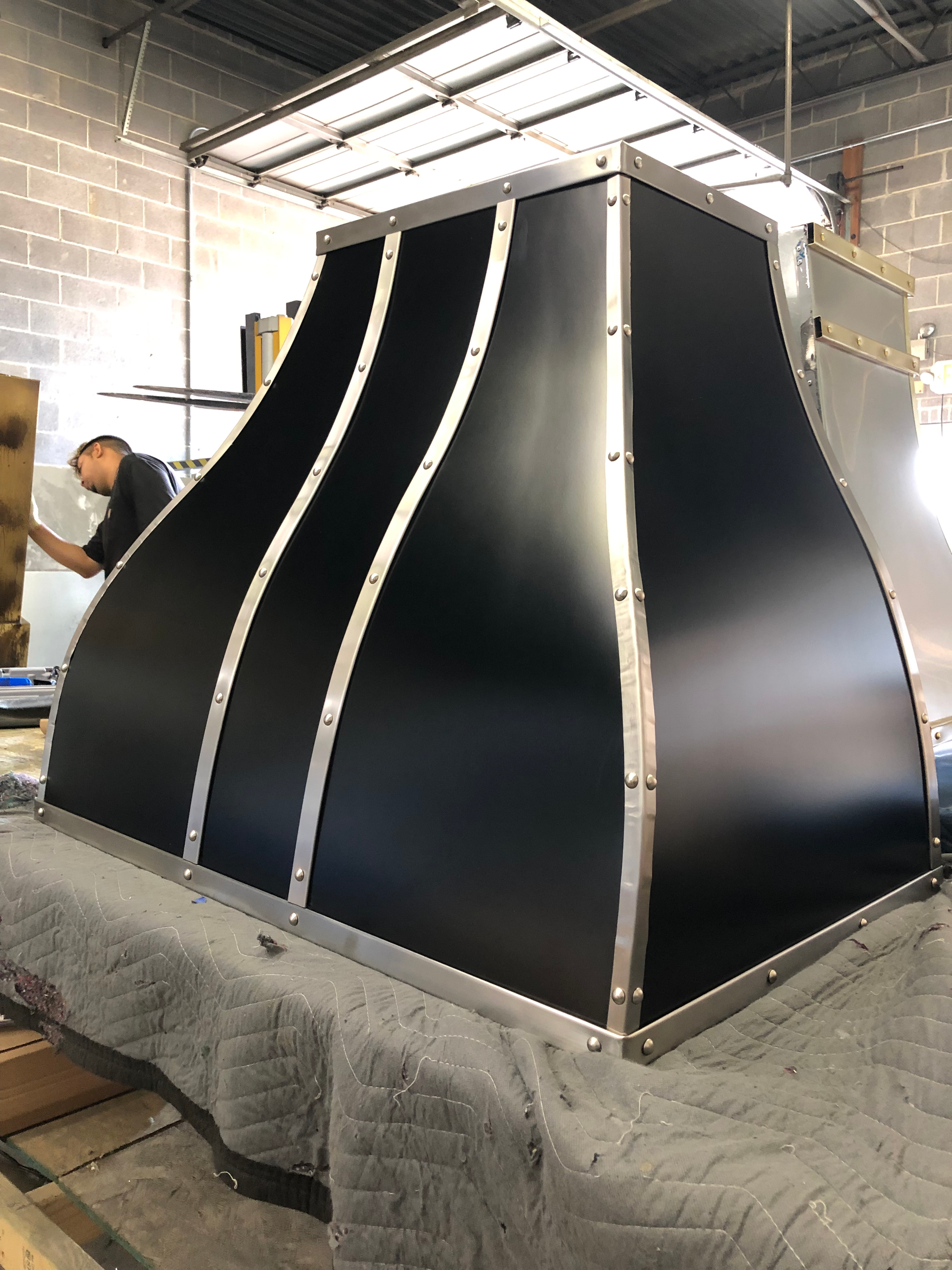 A man is working on a black and silver hood in a factory.