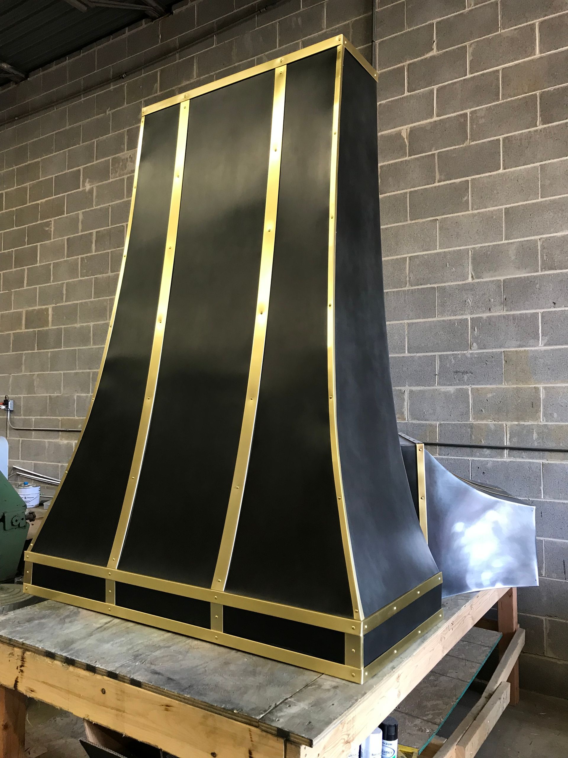 A black and gold hood is sitting on a wooden table in front of a brick wall.