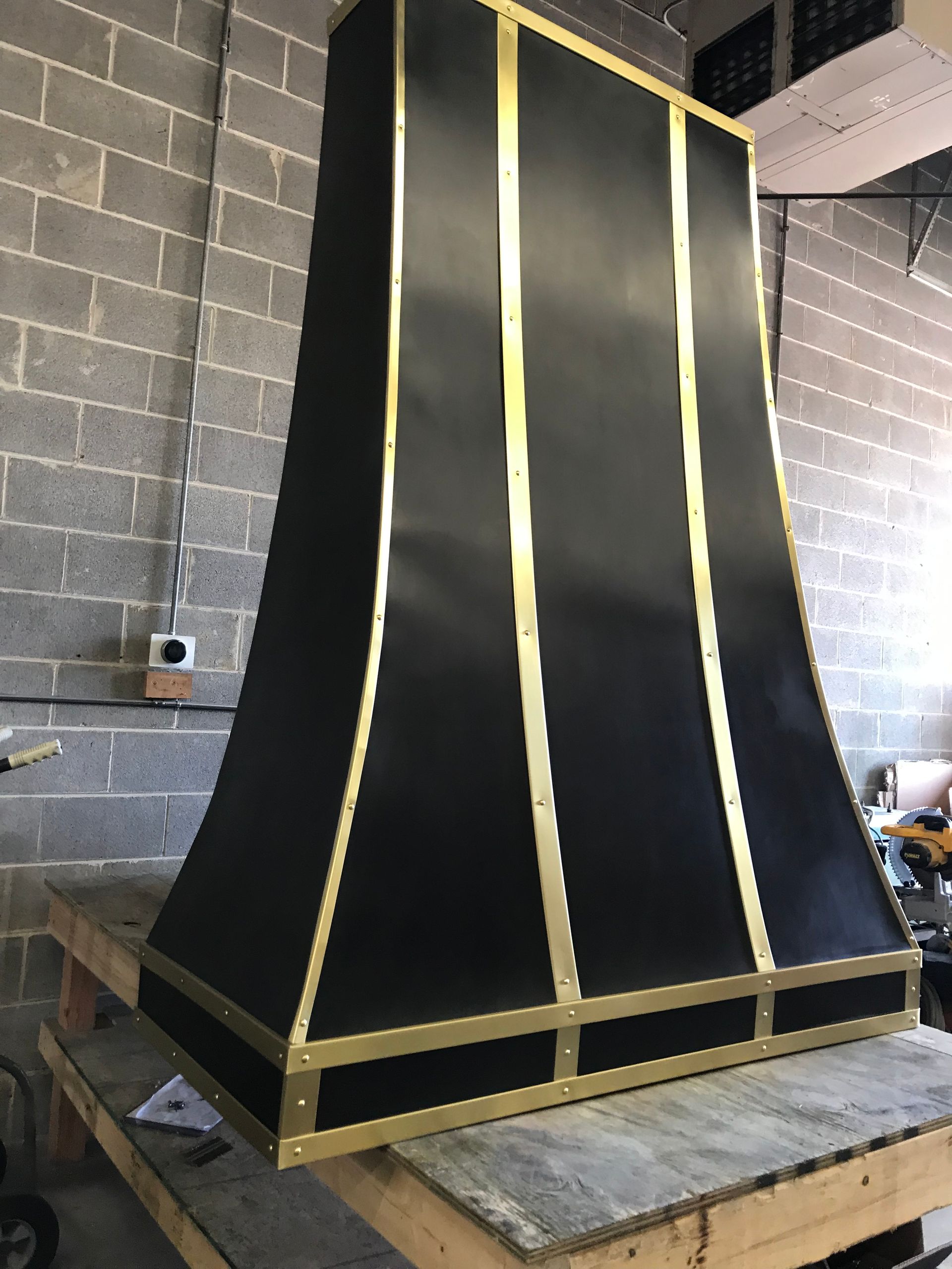 A black and gold hood is sitting on a wooden table in front of a brick wall.